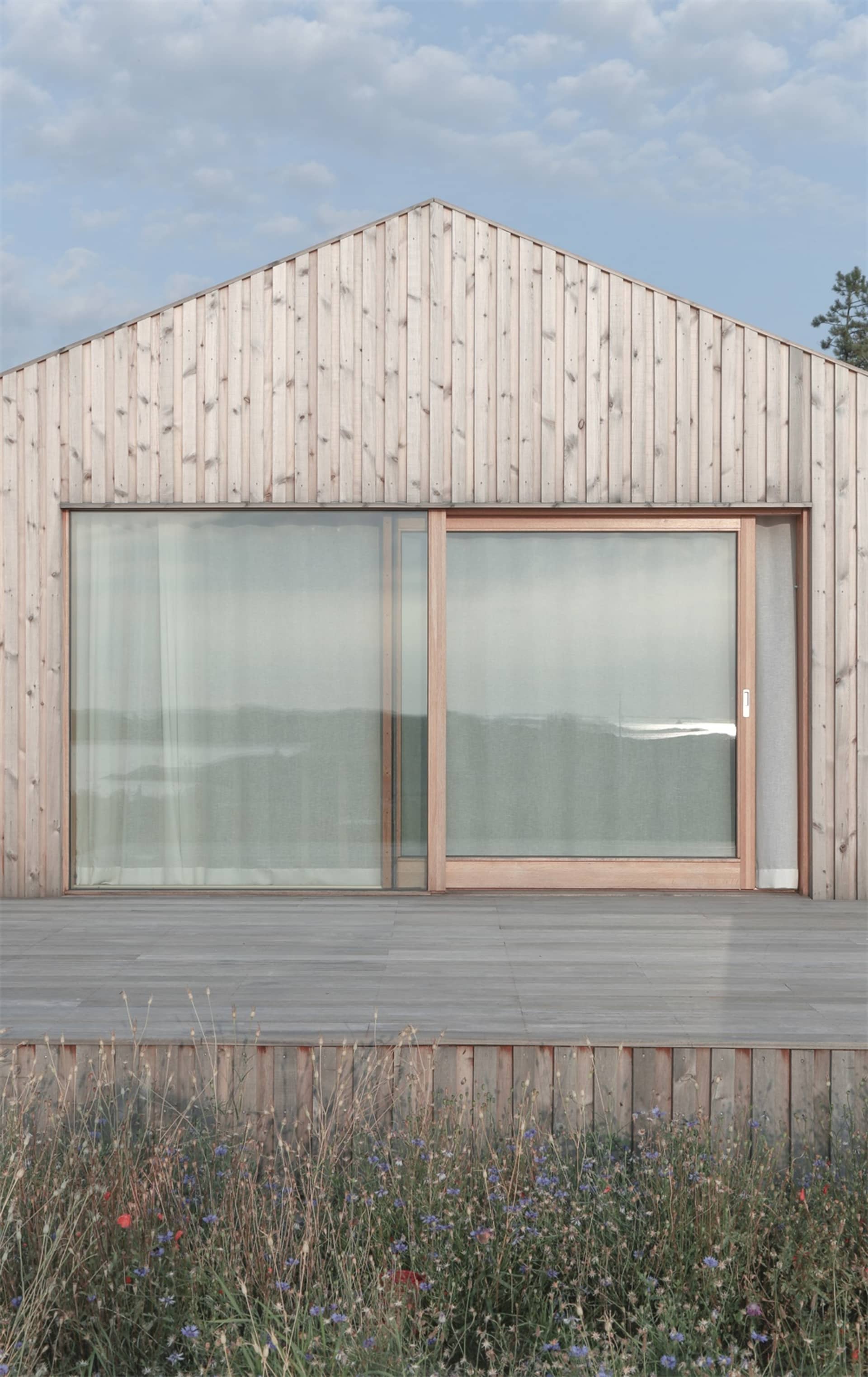 A modern residential exterior with large glass windows and a wooden panel roof.