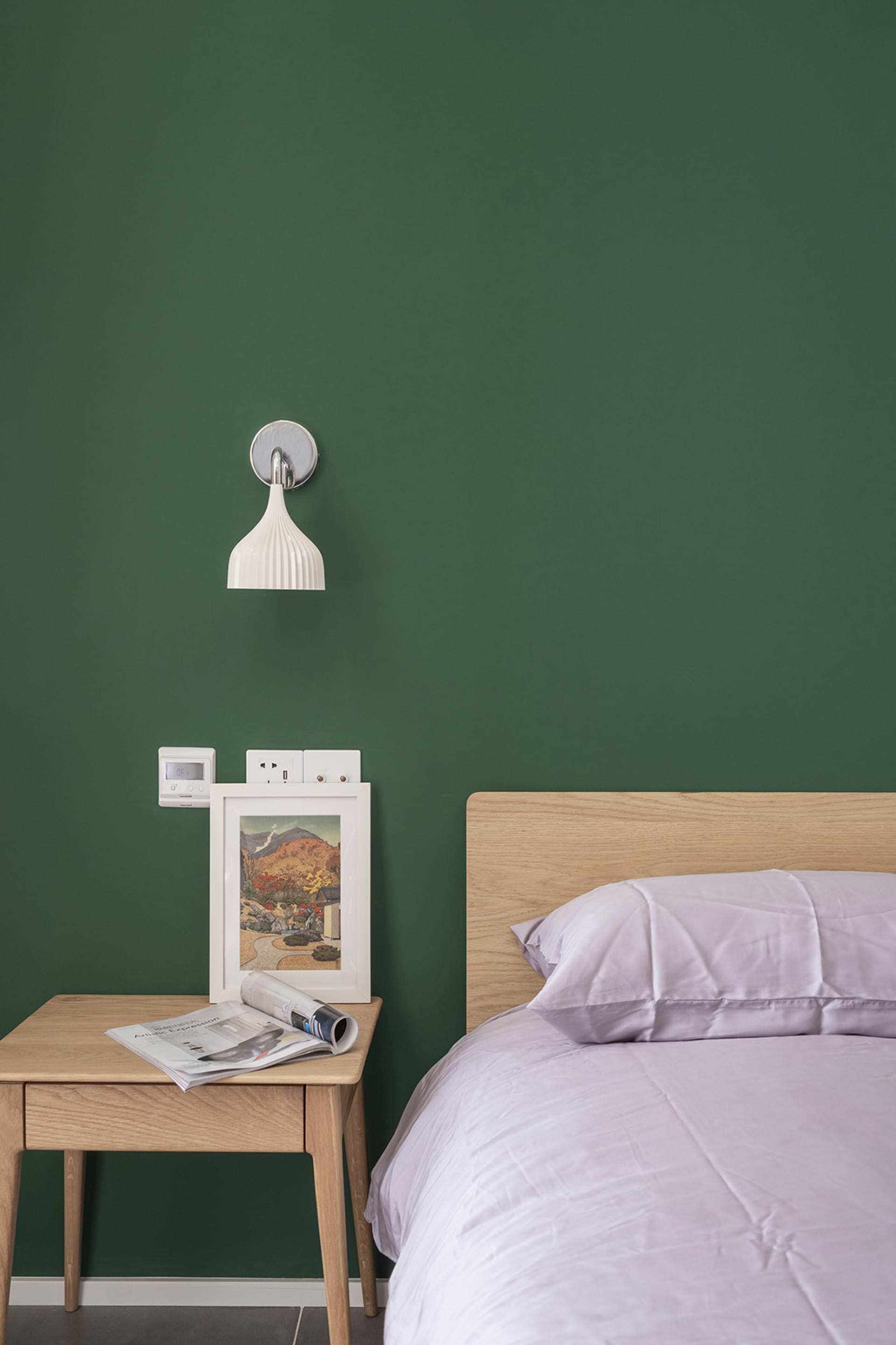 A minimalist bedroom with a wooden headboard on a green wall, featuring a bed with white bedding and a side table with a fram