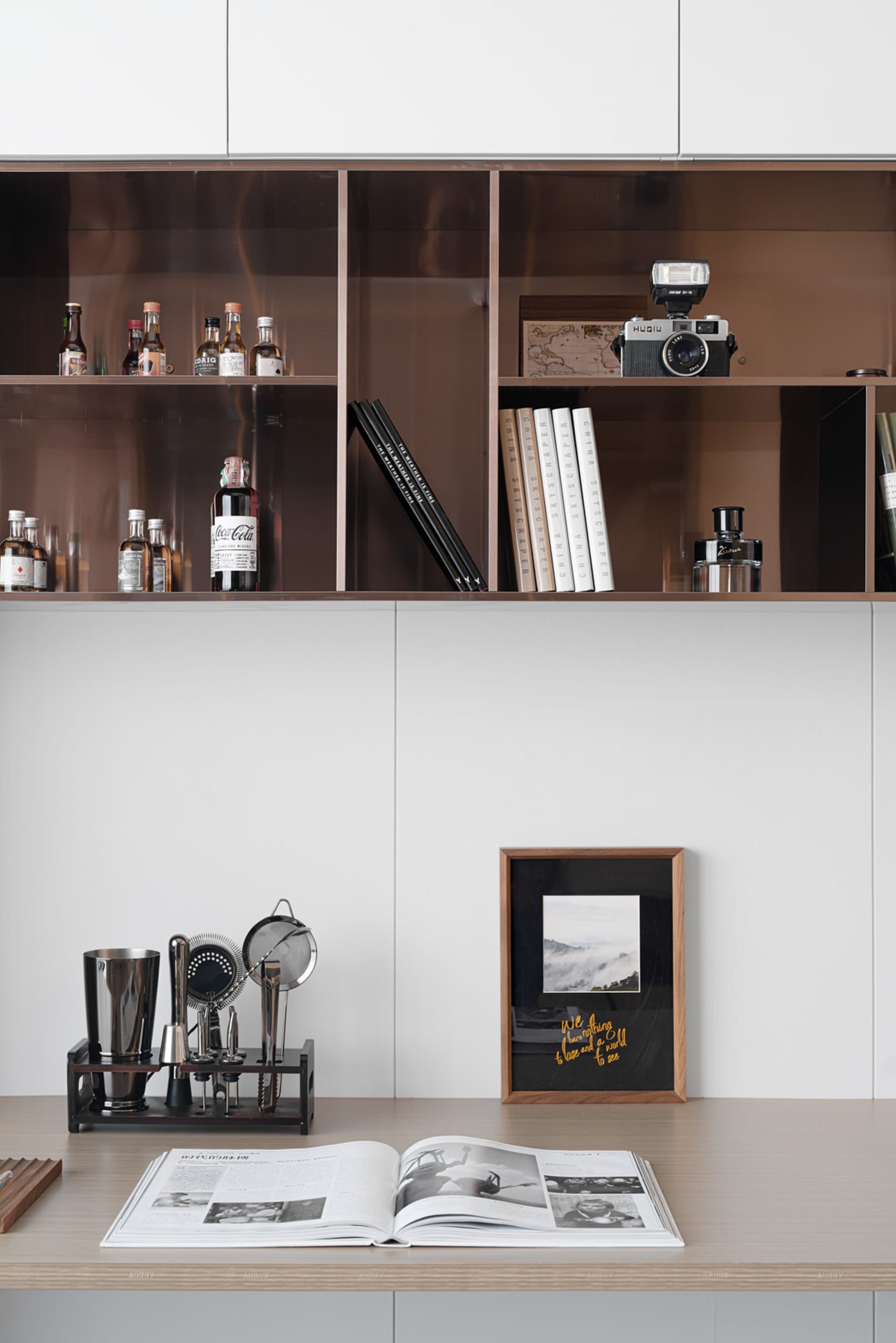 A modern minimalist home bar with wooden shelves filled with bottles, books, and a camera, along with a wooden frame and a ma