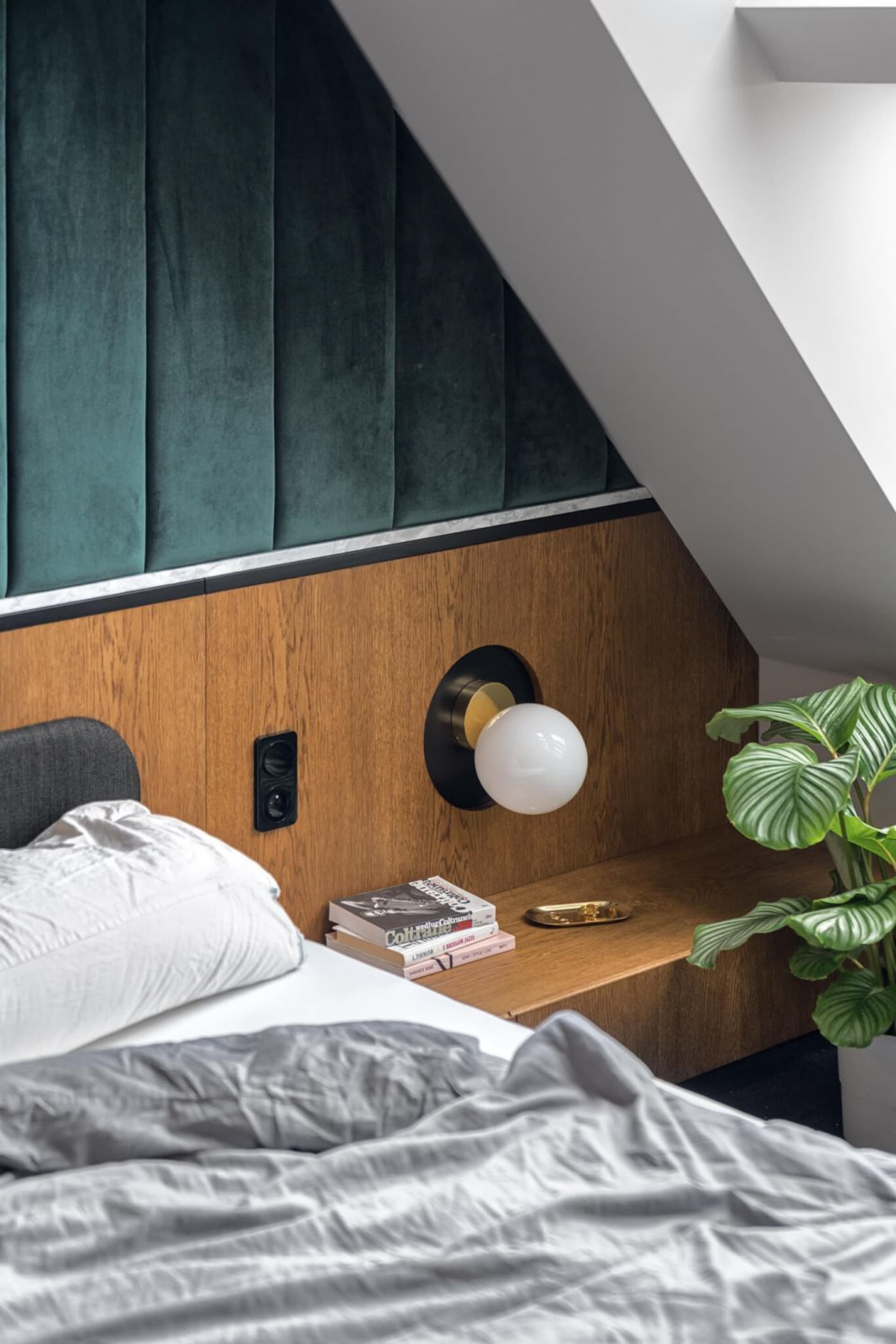 A modern bedroom with a green velvet headboard and wooden accents.