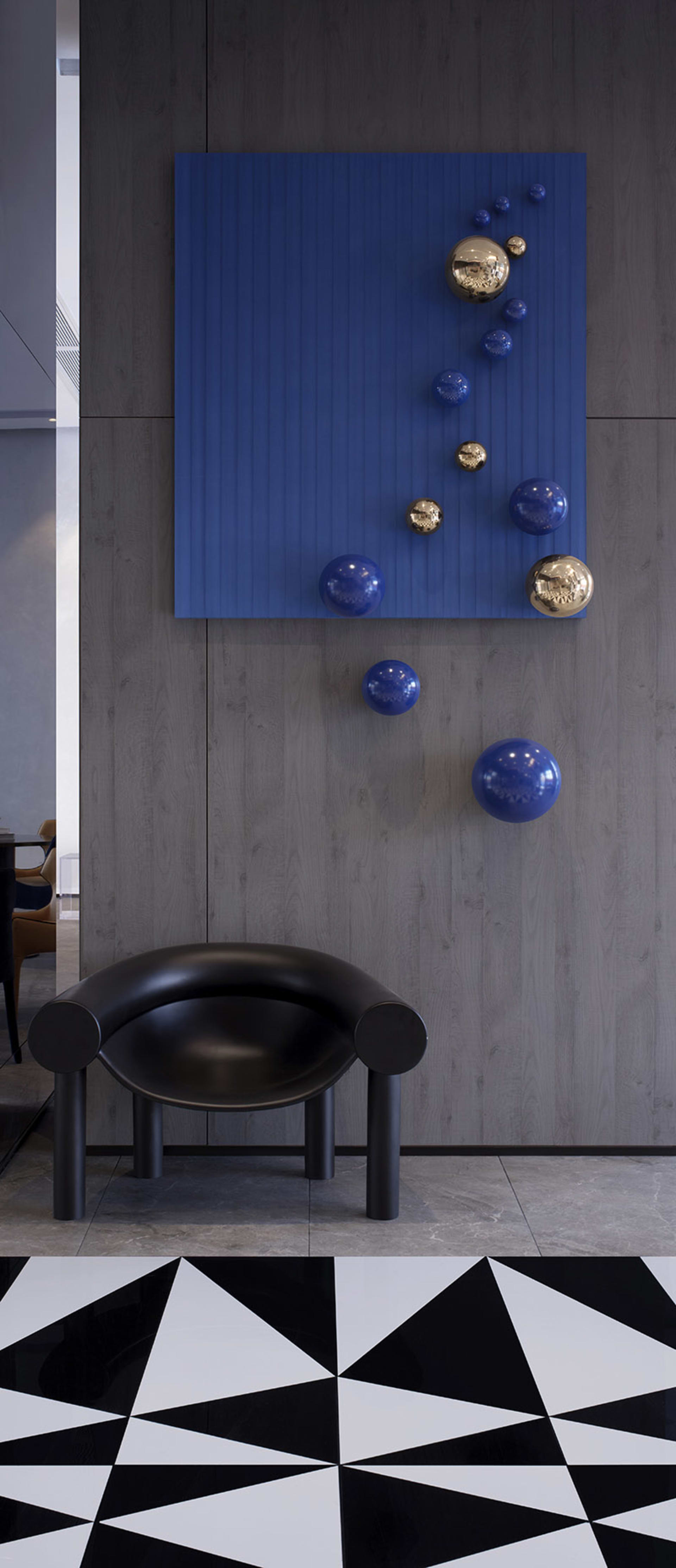 A sleek black curved chair with blue resin spheres hanging on the wall in a modern lobby setting.