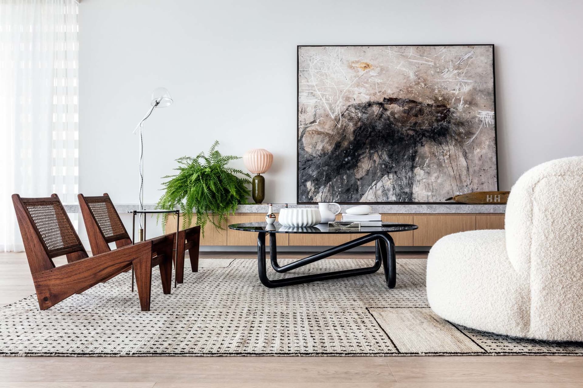 Modern living room with wooden chairs, leather sofa, metal coffee table, and abstract painting.