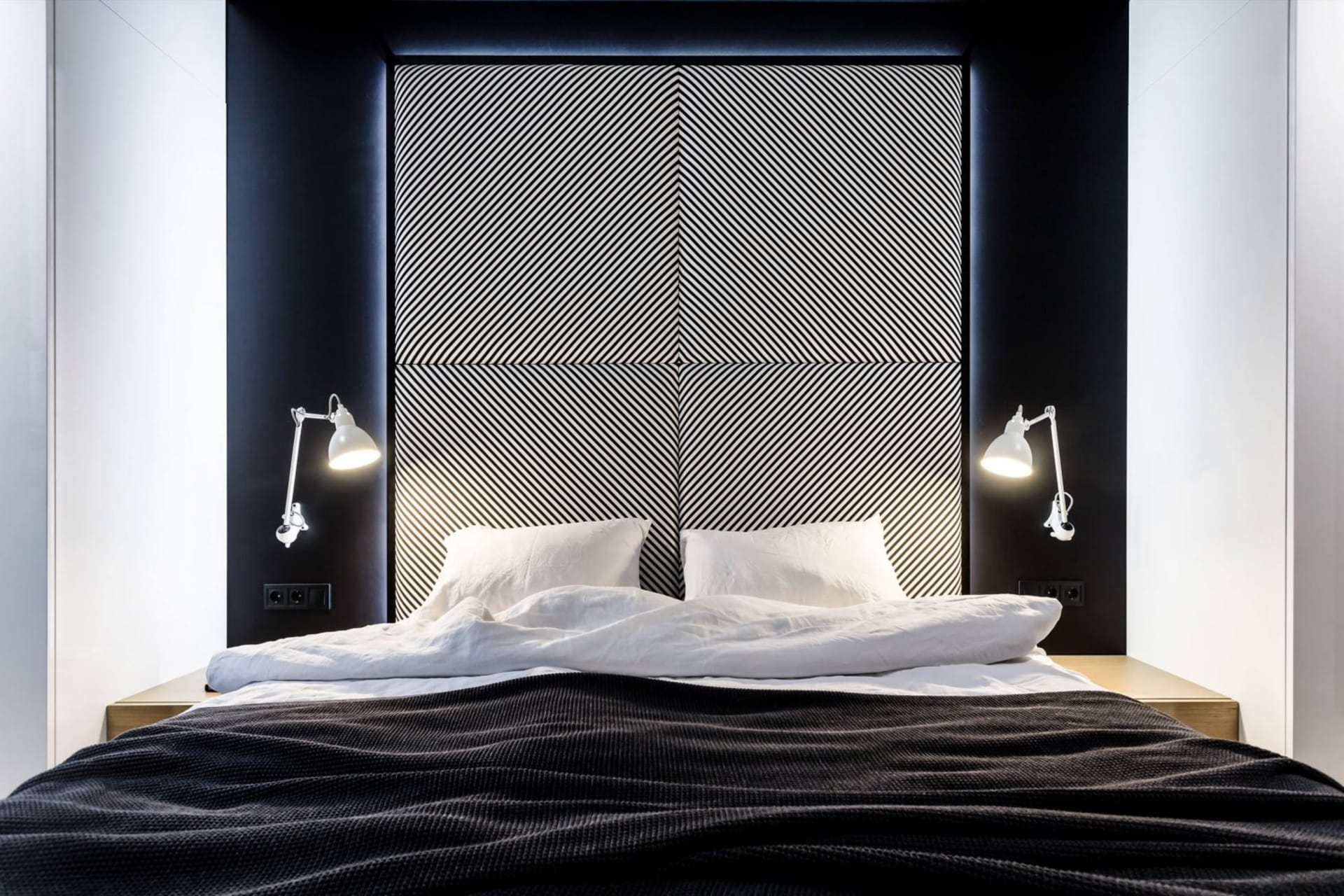 A modern minimalist bedroom with a textured fabric headboard and nightstands with white lamps.