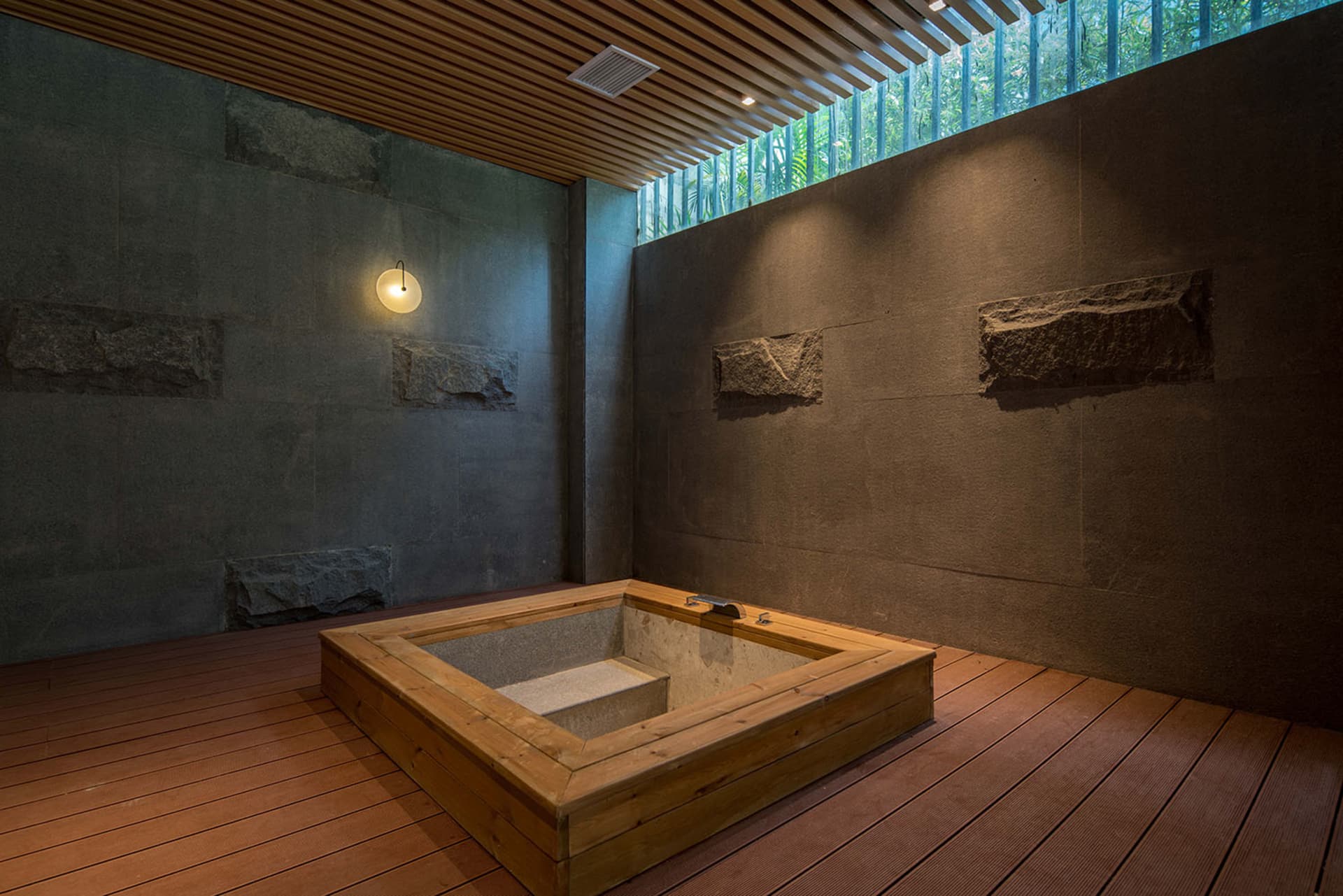 Modern minimalist interior with a hot tub in a stone and wood terrace setting.