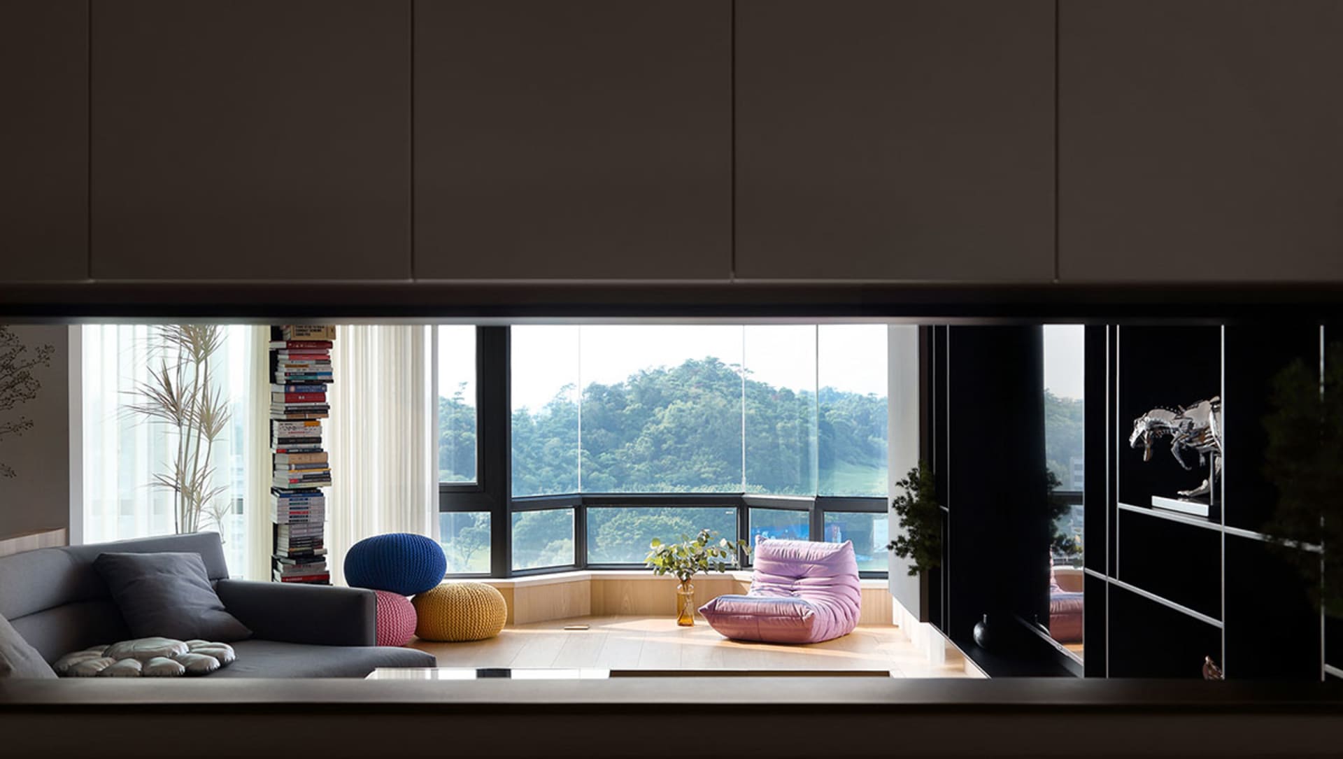 A modern living room with wooden flooring, glass walls, and colorful fabric seating and decorations.