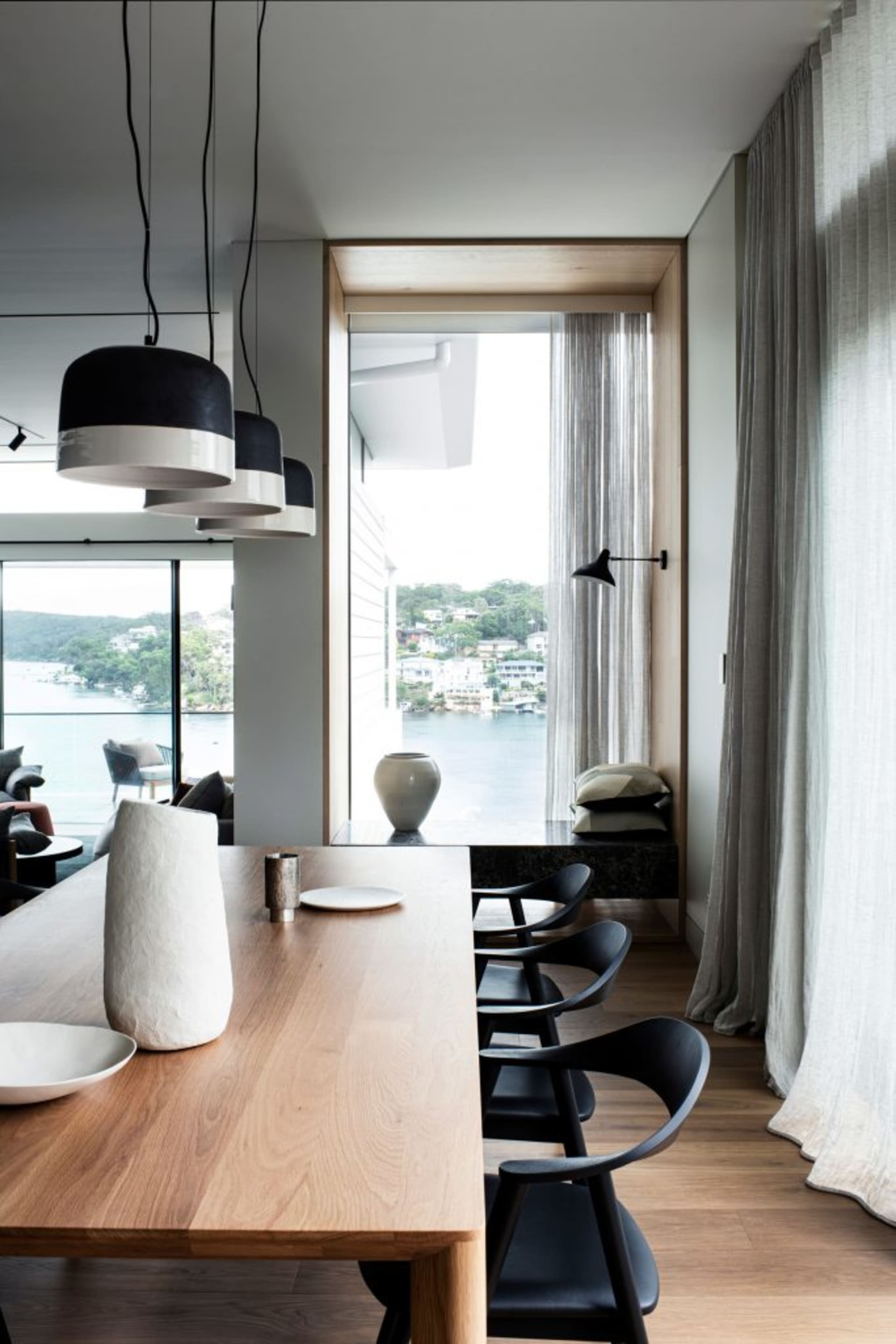 A modern dining room with a view of the water, featuring wooden furniture and minimalist decorative elements.