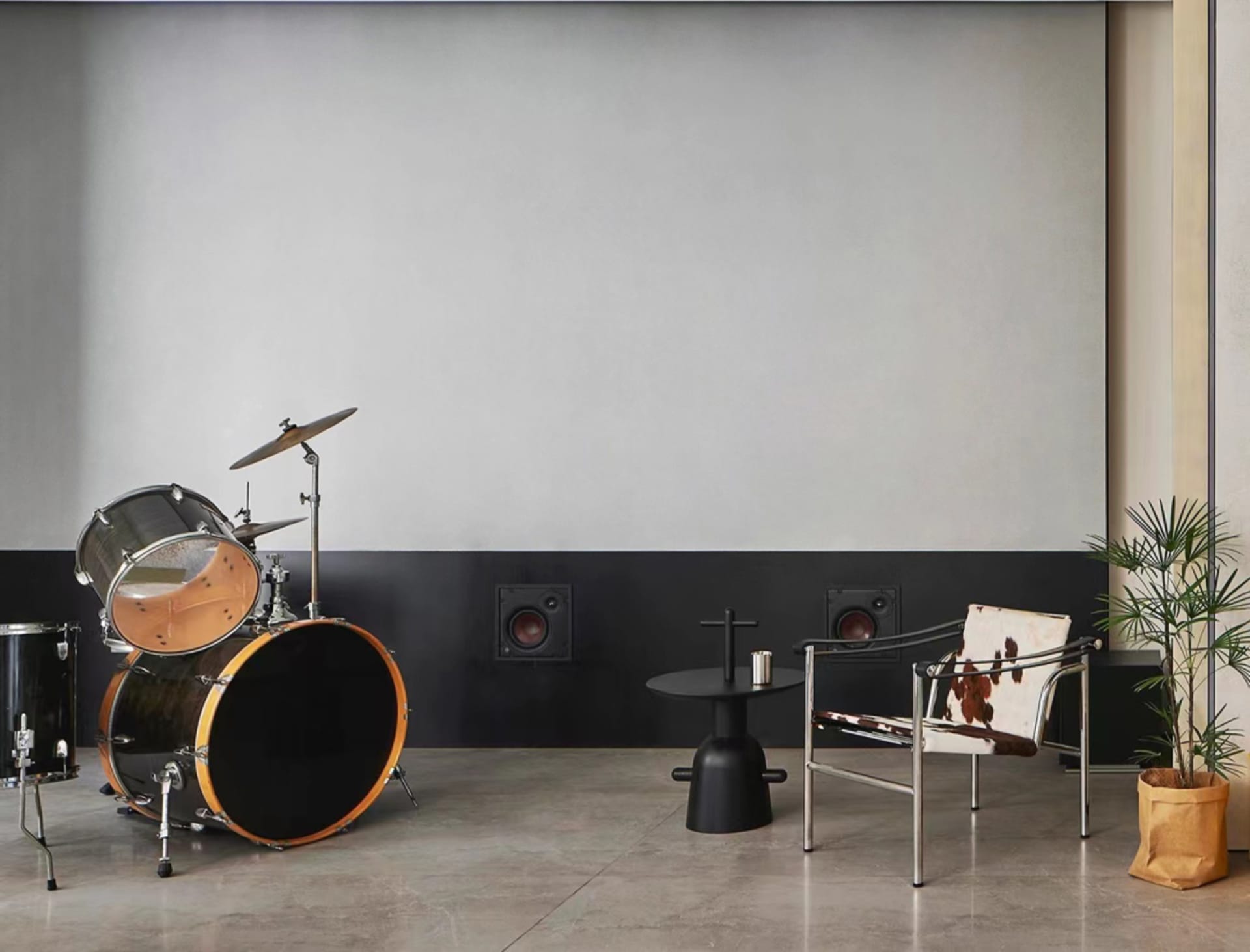 A modern music room featuring a black drum set, a chair with a cowhide cushion, and a plant in a paper bag.