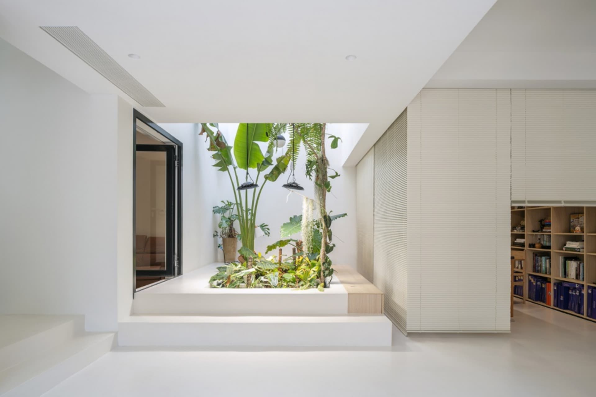 A modern interior space featuring a plant-filled box on a raised concrete platform, with green plants, hanging plants, and a