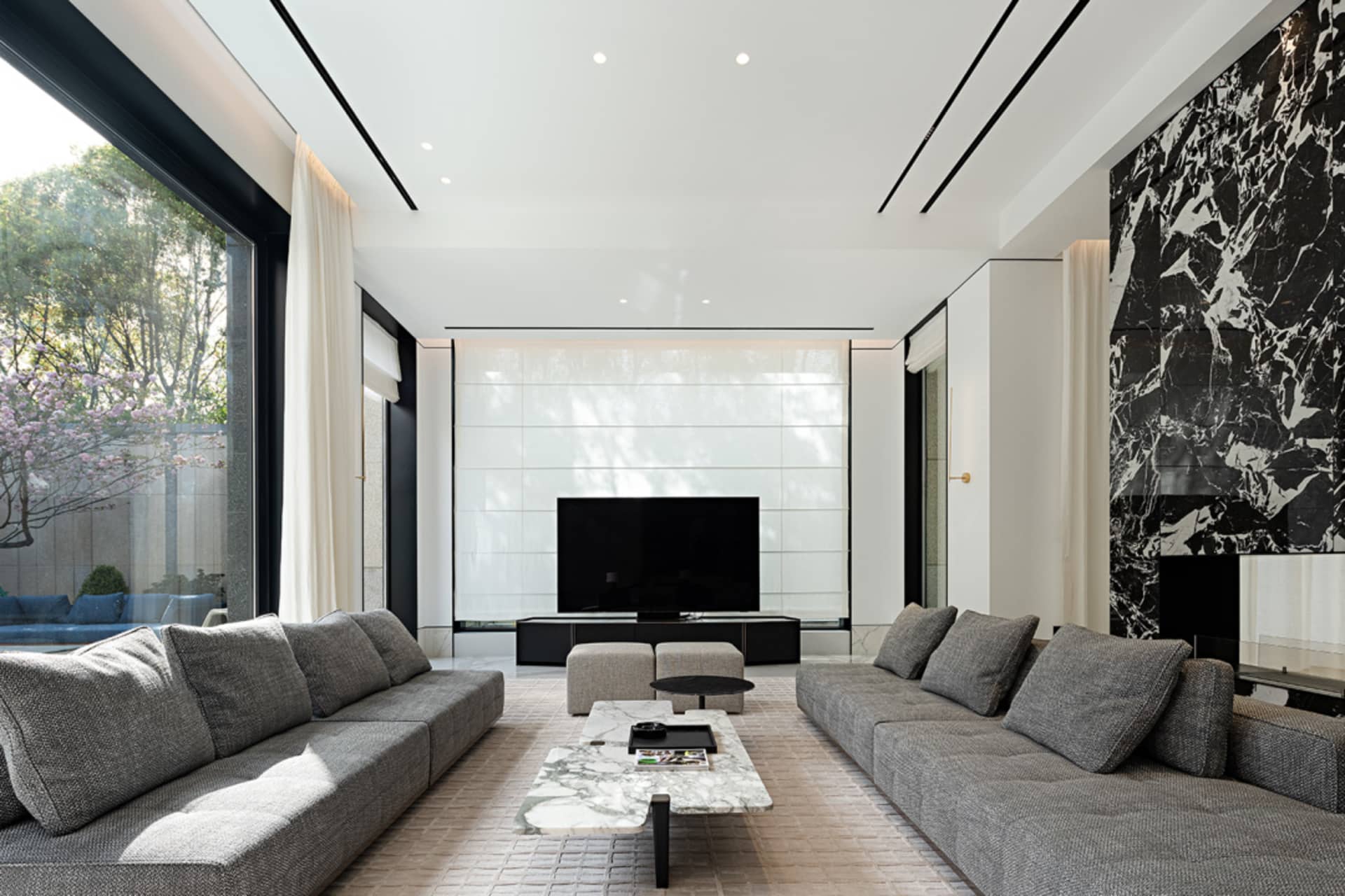 A modern living room with a marble coffee table, gray sofas, and a large screen television.