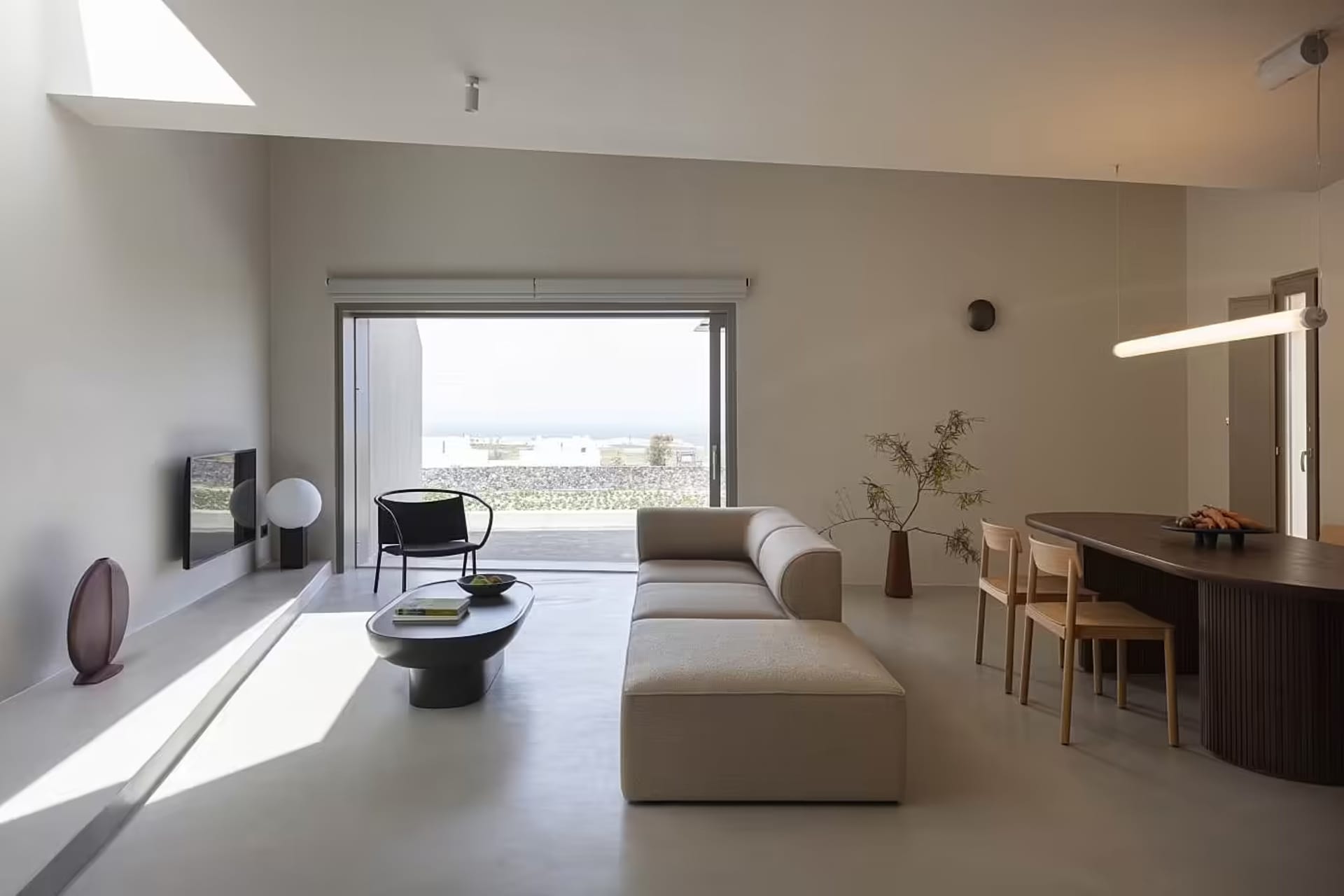 Modern minimalistic living room with concrete flooring, a white couch, and a large window overlooking an ocean view.