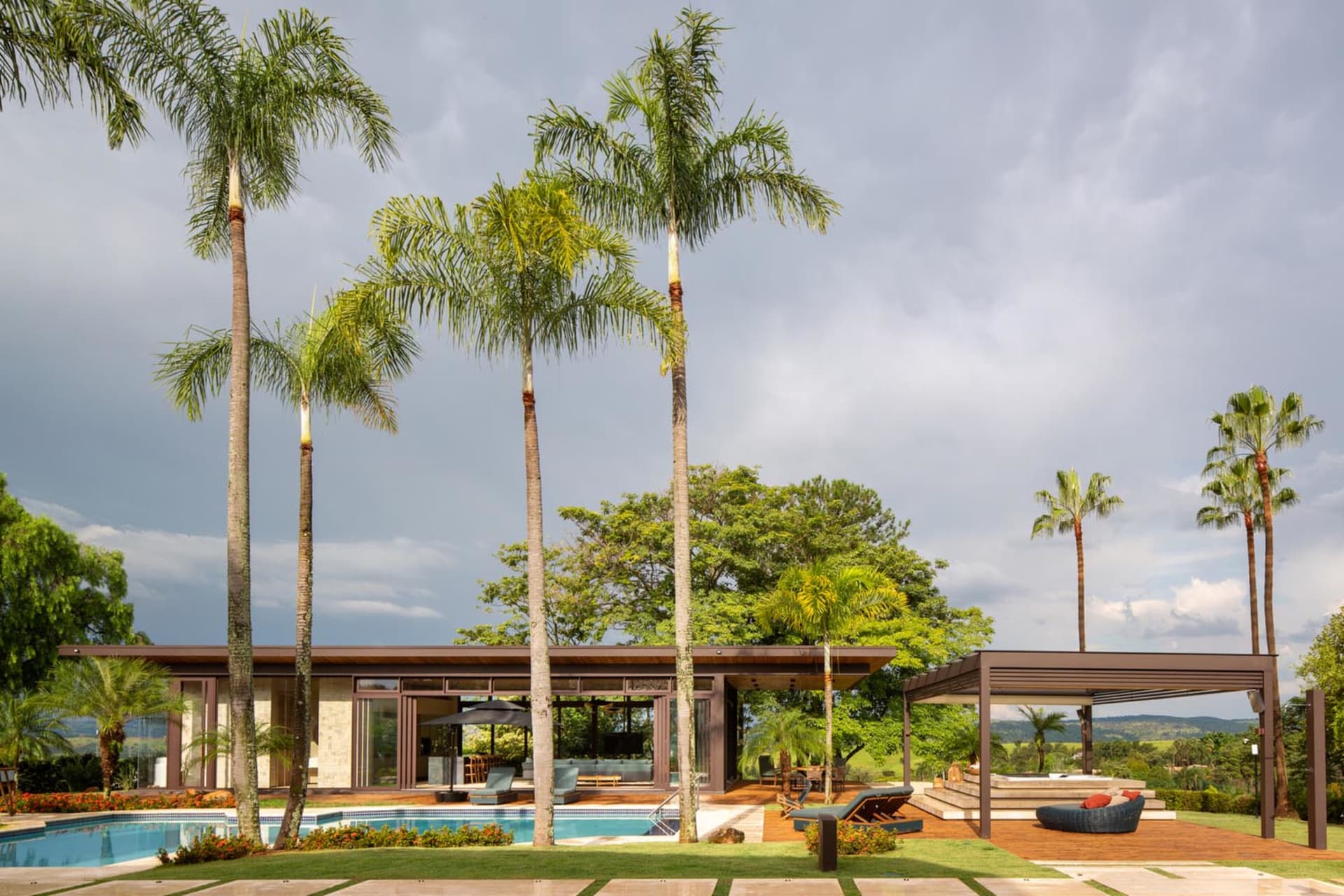 Modern house exterior featuring a pool surrounded by palm trees and lush greenery.