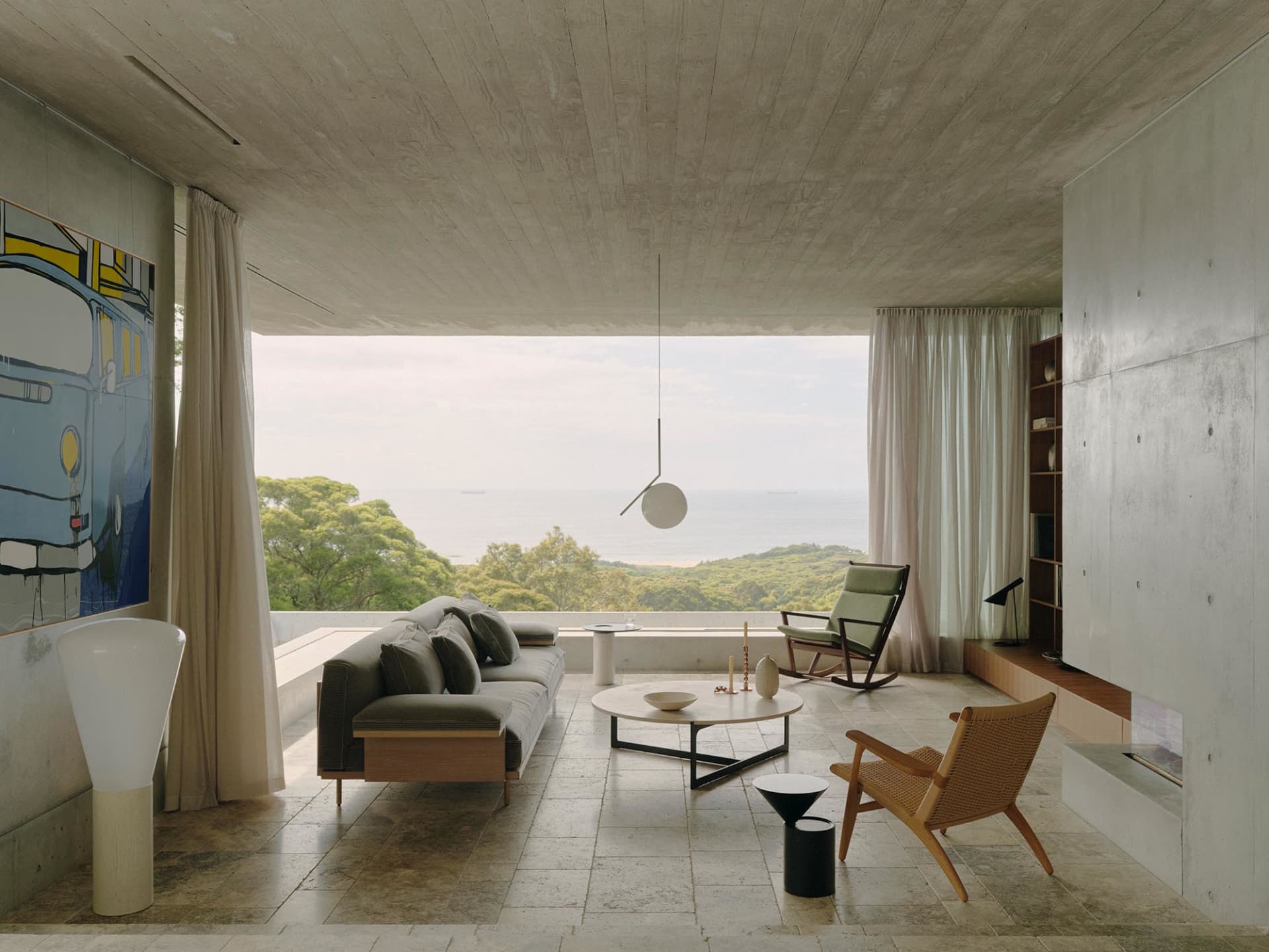 A minimalist living room with a concrete floor, a large window, a green rocking chair, and a green rug.