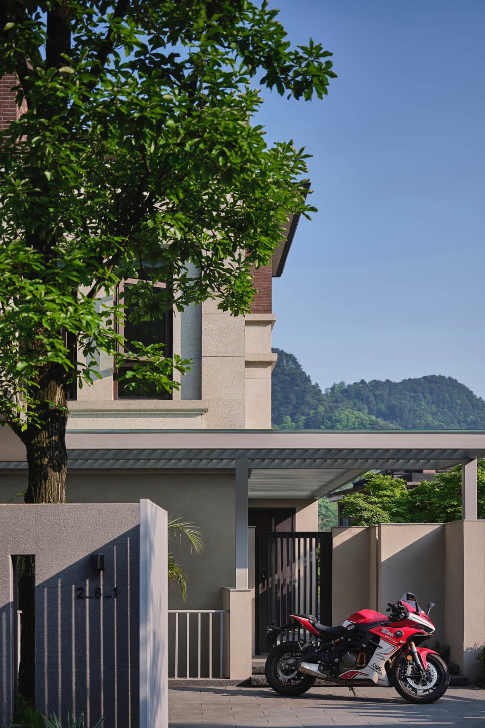 A modern residential exterior with concrete walls and a lush tree nearby.