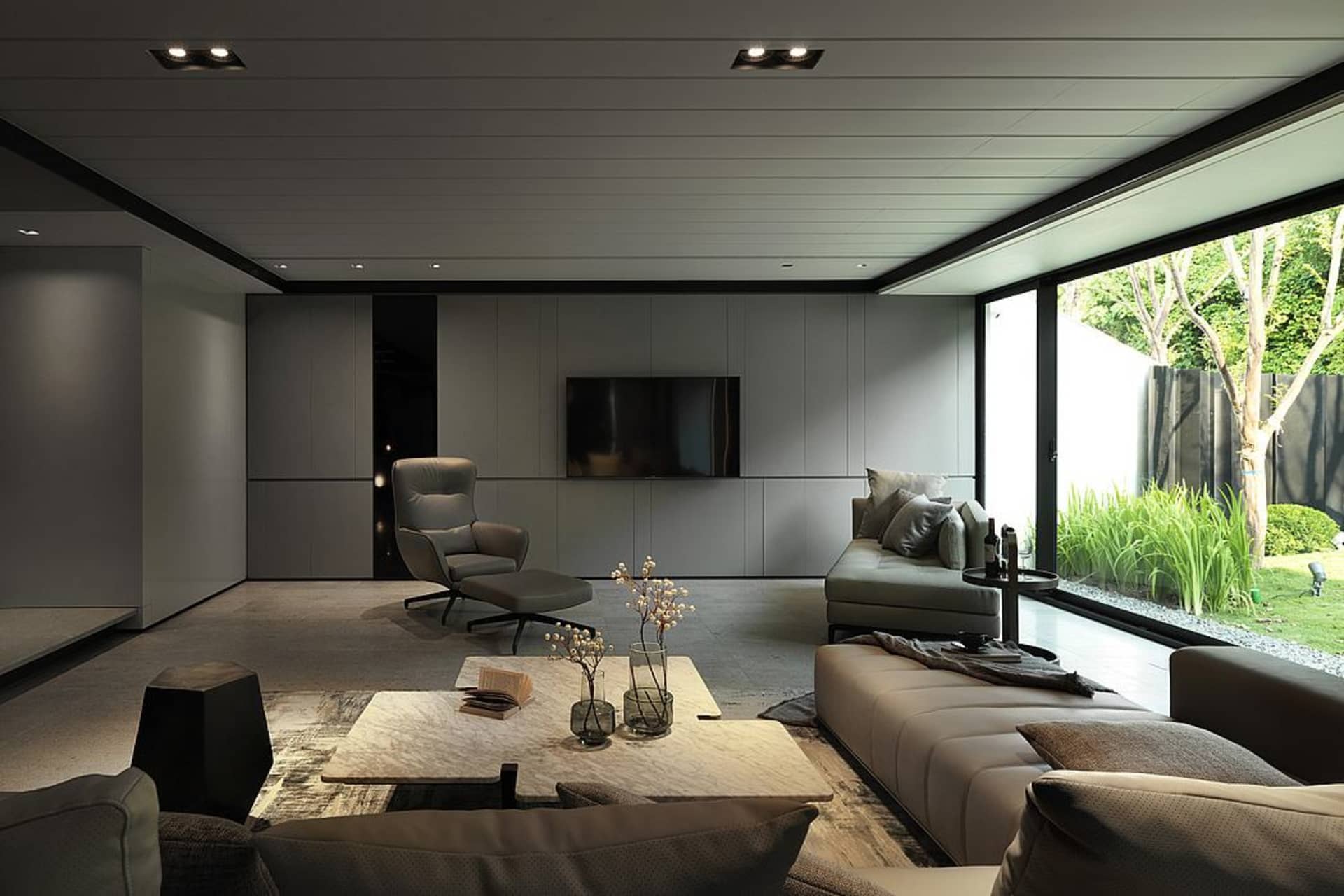 A modern minimalist living room with grey concrete walls, a large window, and contemporary furniture.