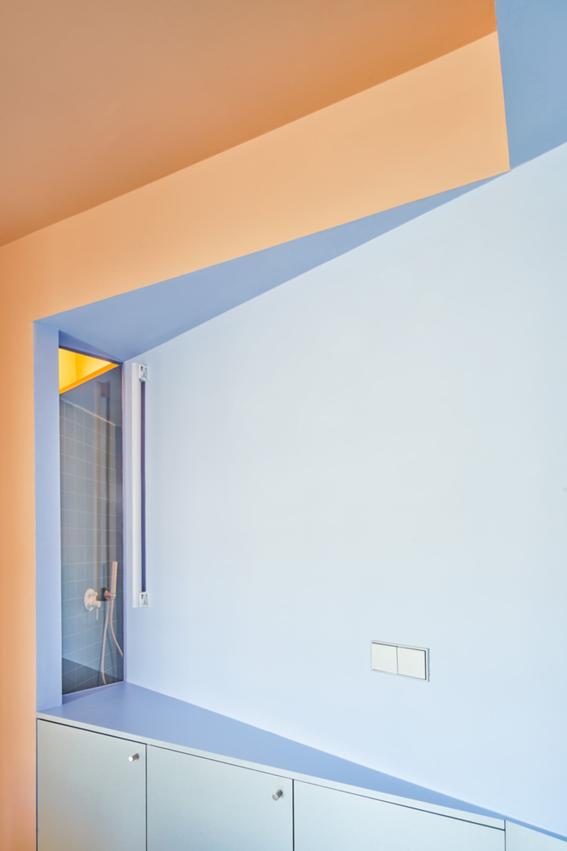 Modern bathroom with glass shower enclosure, minimalist design, light blue walls, and orange ceiling trim.