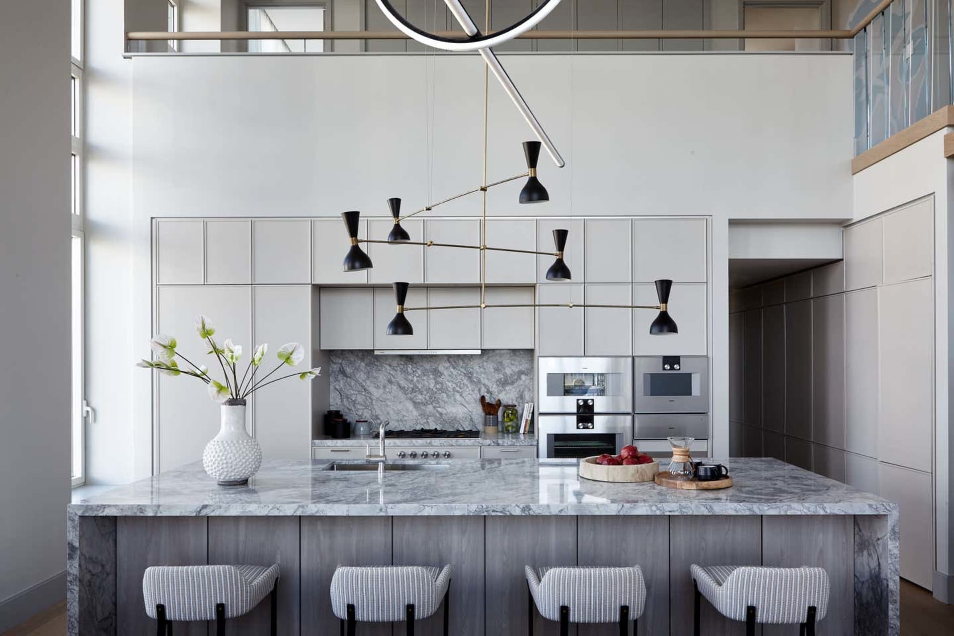 An elegant, modern kitchen with a marble countertop and industrial lighting fixture above a white kitchen island with seating