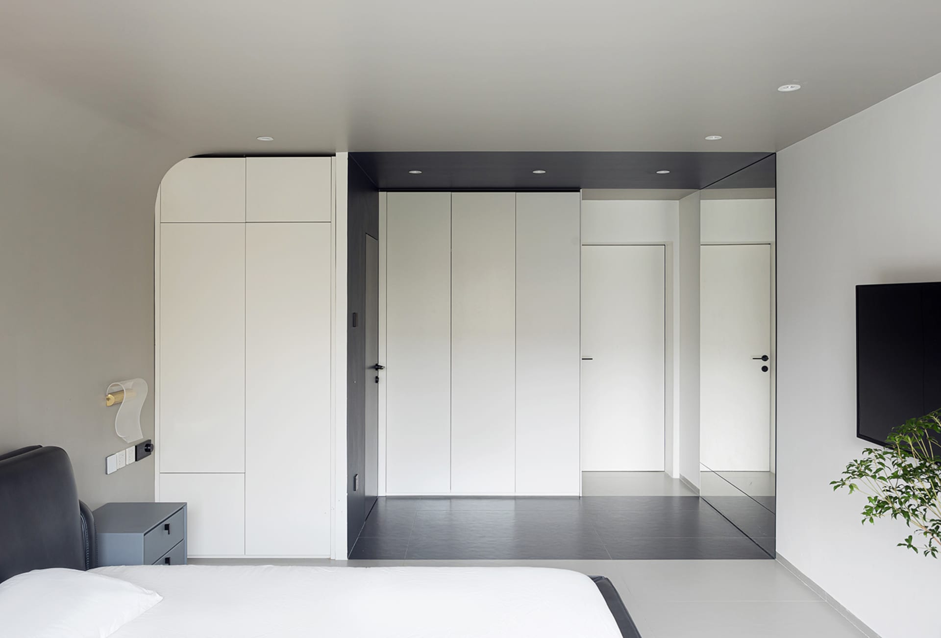 A modern minimalist bedroom with white walls, a black headboard bed, and a minimalistic design.