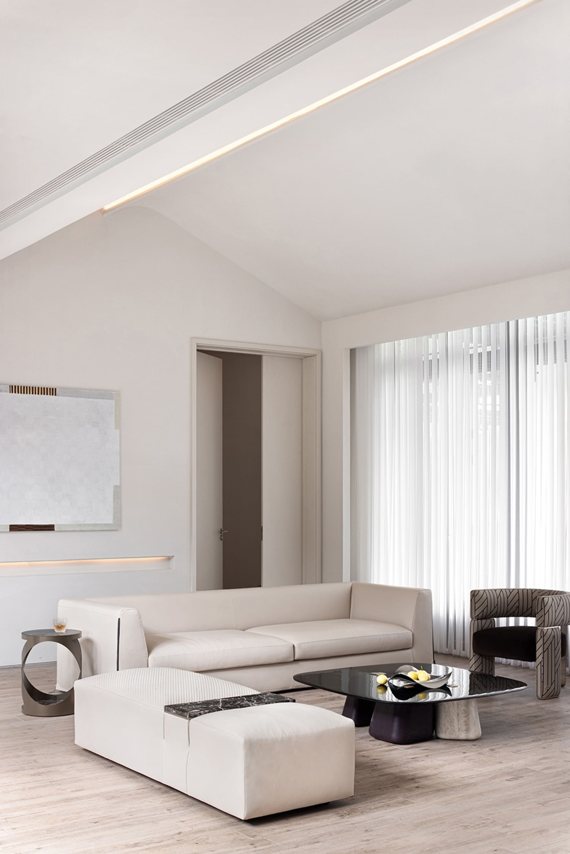 A minimalist living room with white leather furniture, a glass coffee table, and white curtains.