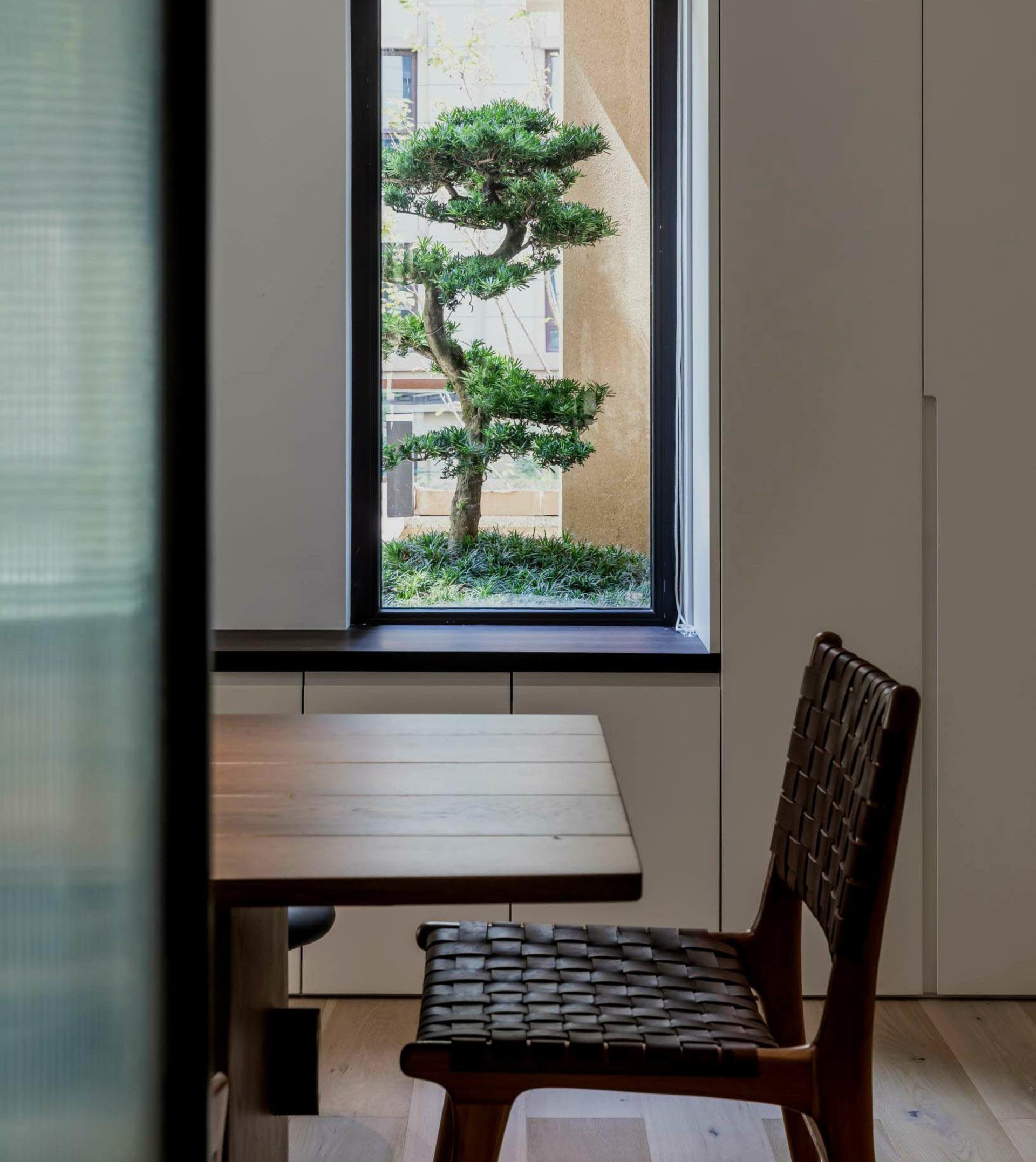 A cozy and modern interior space featuring a miniature bonsai tree on a small wooden table, with white walls and wooden floor