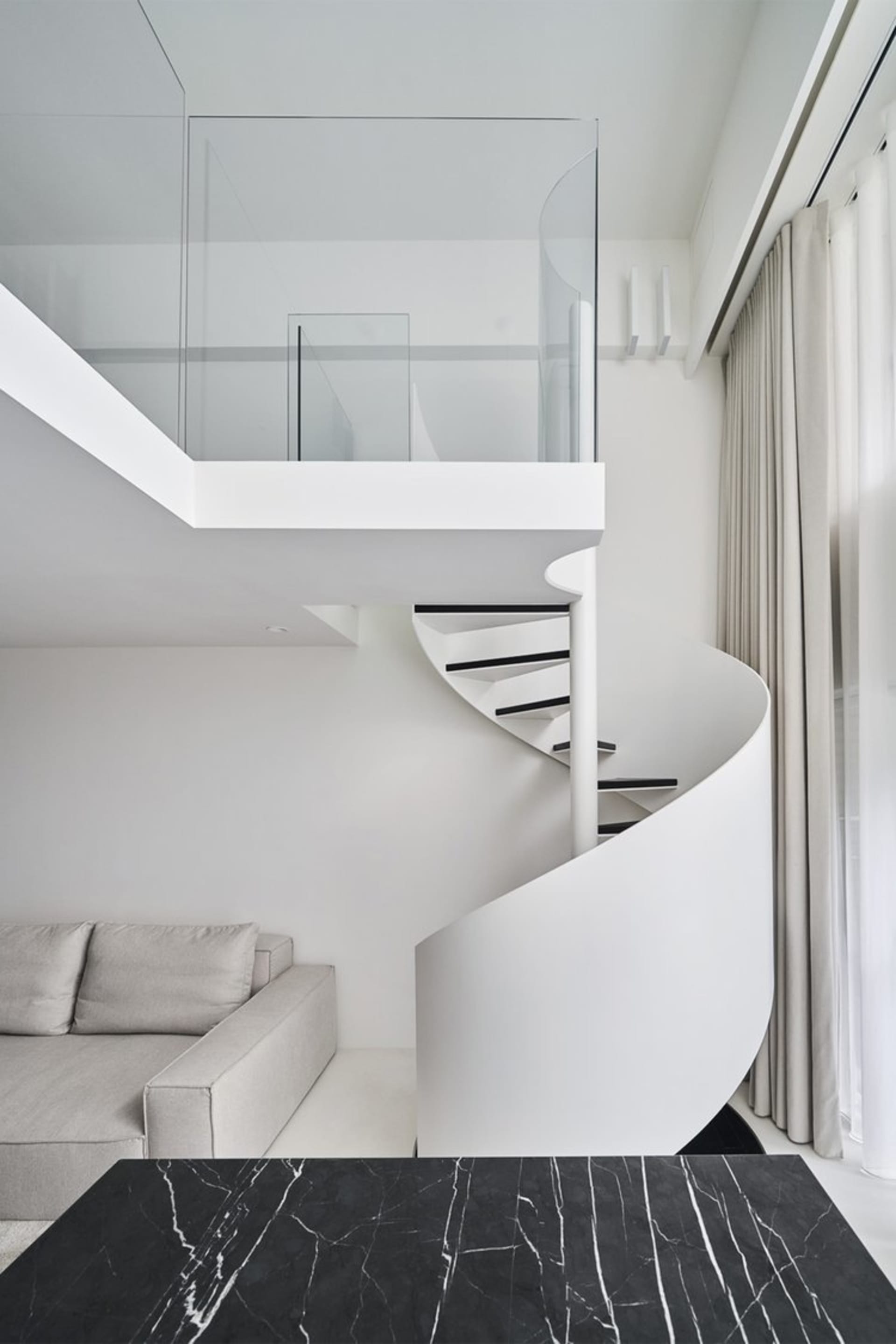 A modern residential interior featuring a spiral staircase with glass railings and white walls.