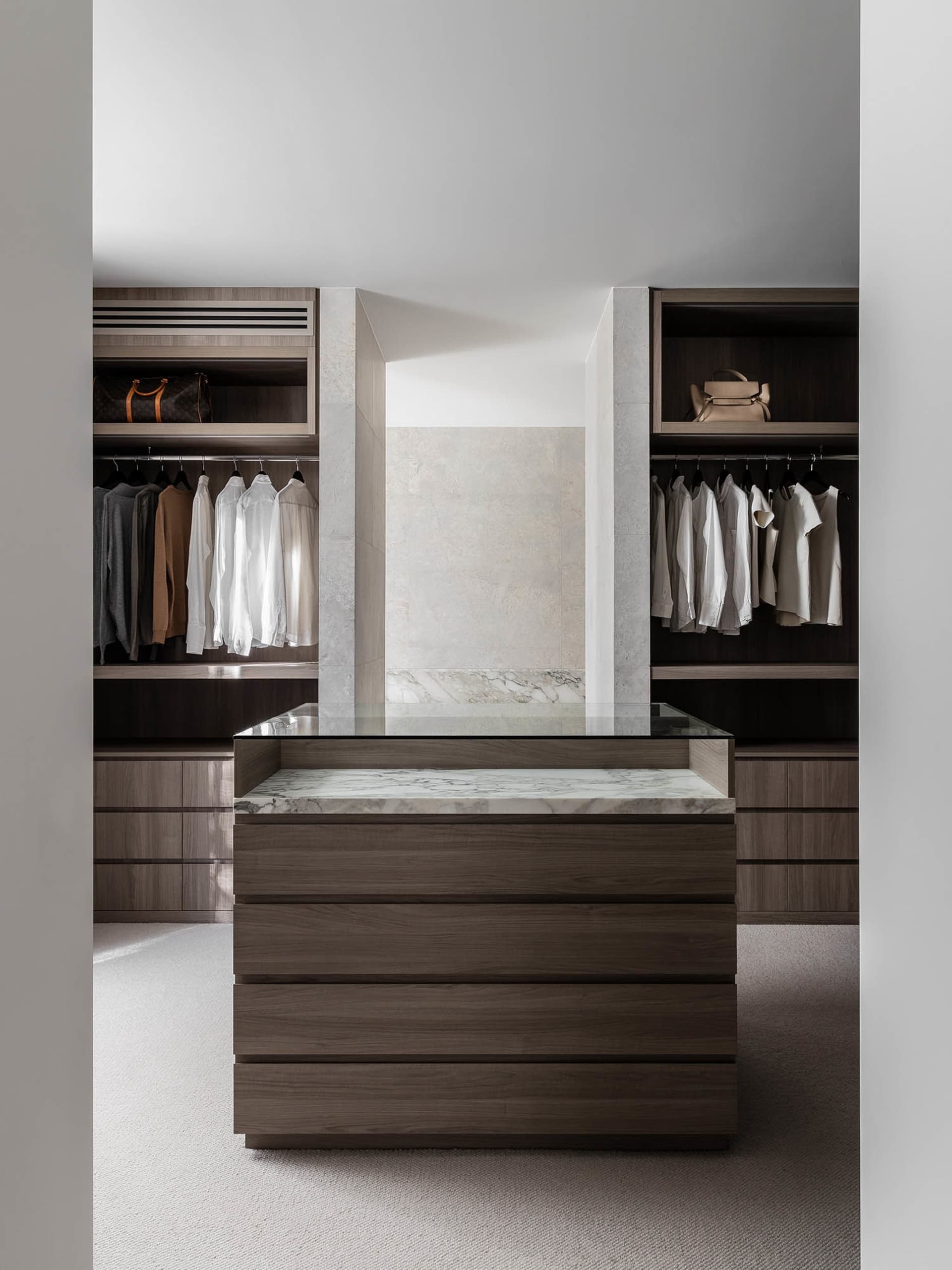 Modern minimalist closet with wood cabinets and marble countertop and shelves.