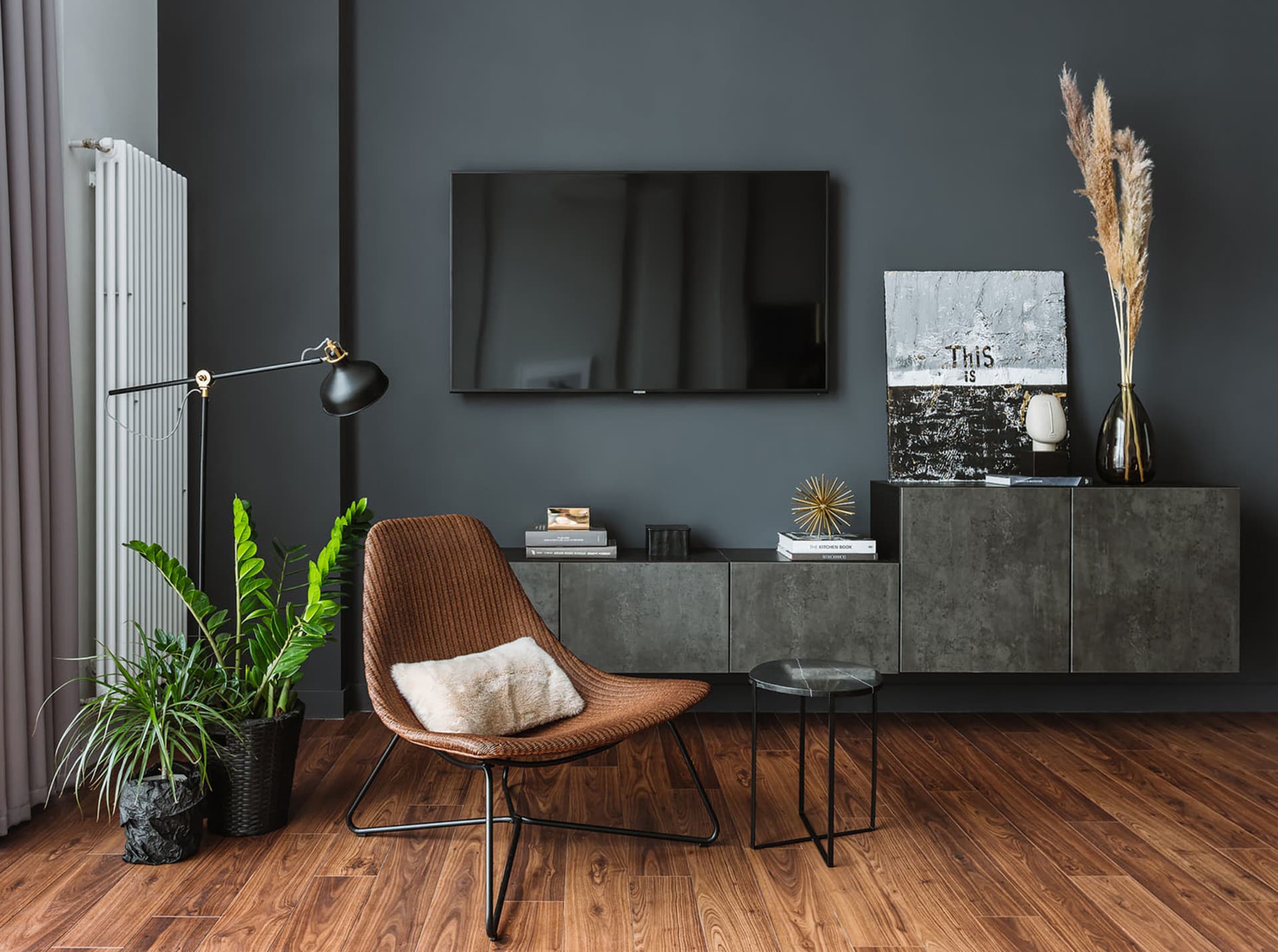 A modern living room with dark gray walls, concrete furniture, and a brown woven chair with a fluffy pillow.