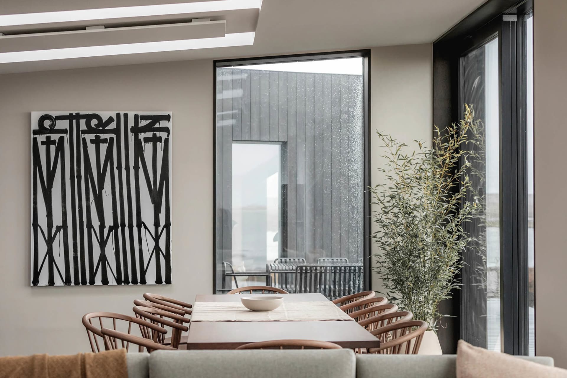 Modern dining room with wooden furniture, large glass windows, and indoor plants.