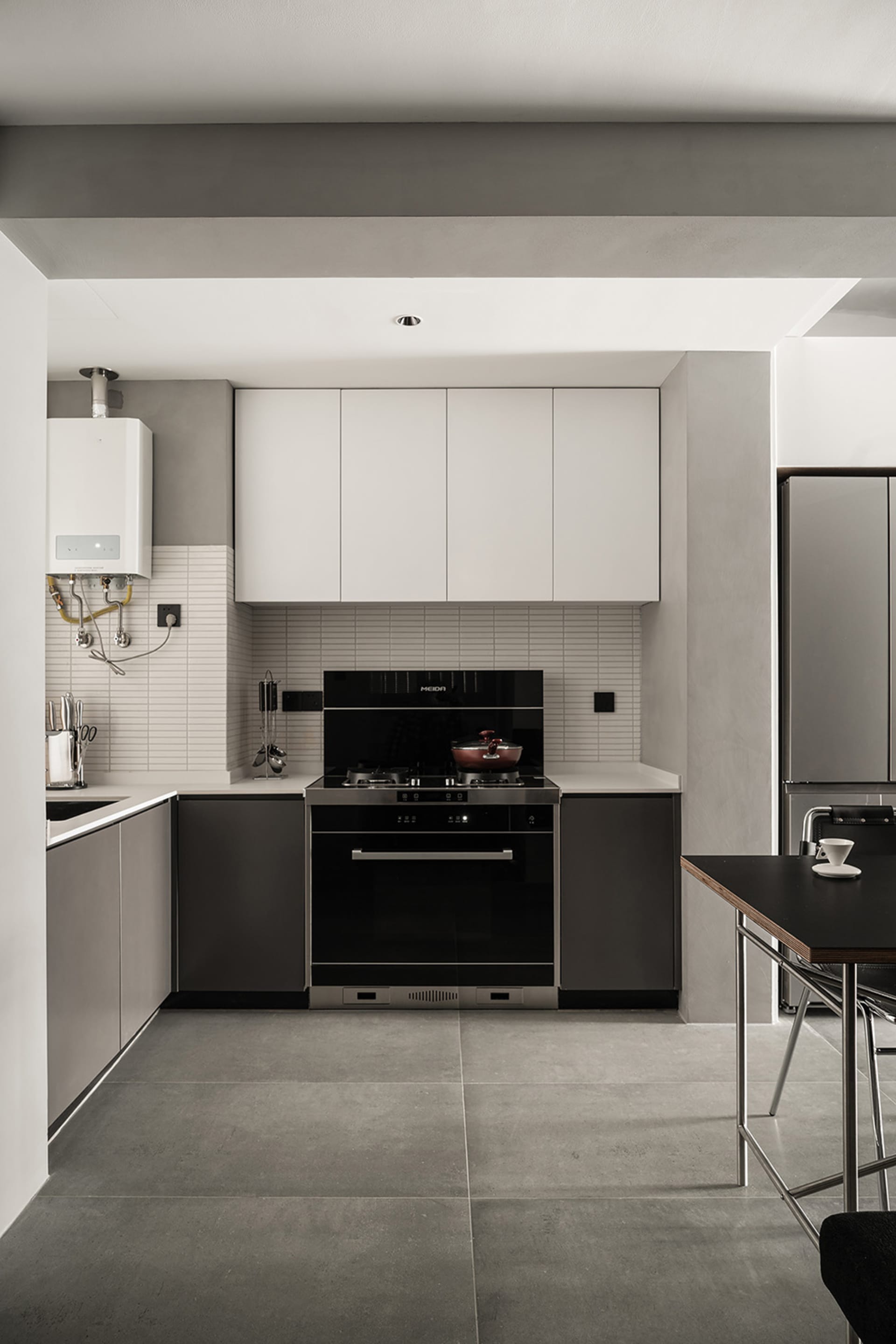 Modern kitchen with concrete flooring, minimalist design, white and black cabinets, and a black stove.