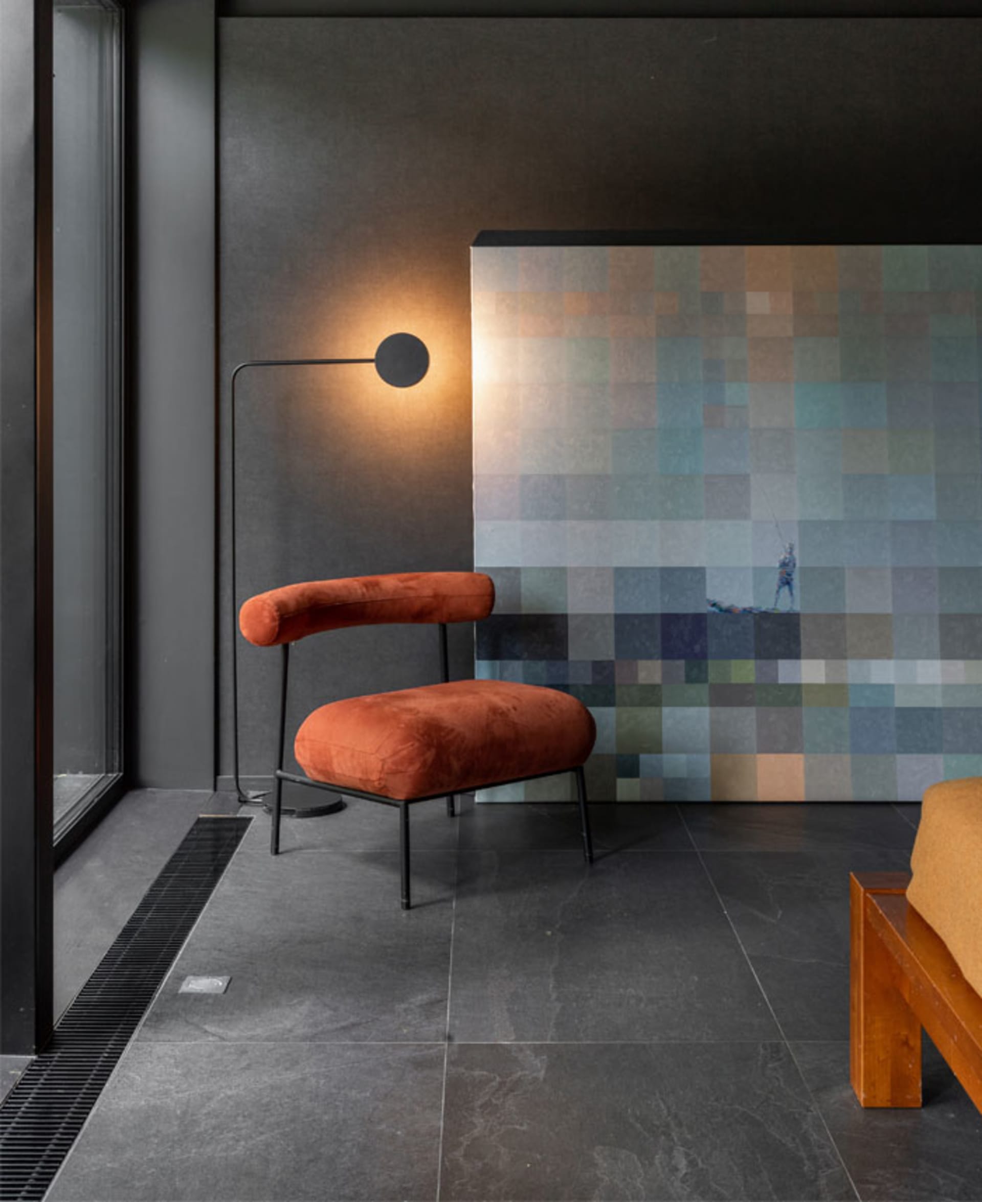 A modern living space featuring an orange velvet armchair with a metal frame, illuminated by a floor lamp in a dark room with