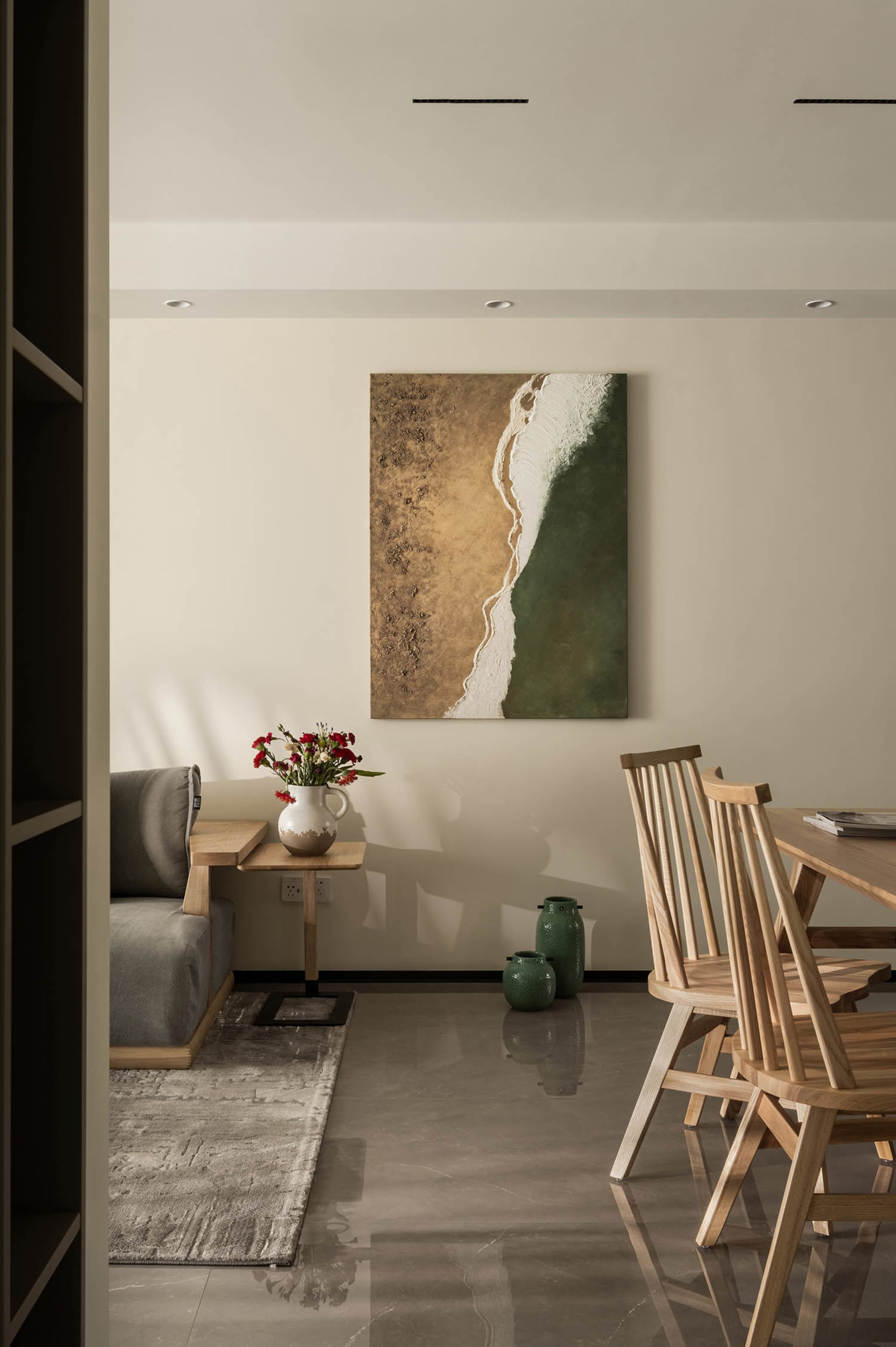 Minimalist dining room featuring wooden chairs, ceramic vases, and a wooden dining table with a beach-themed painting.