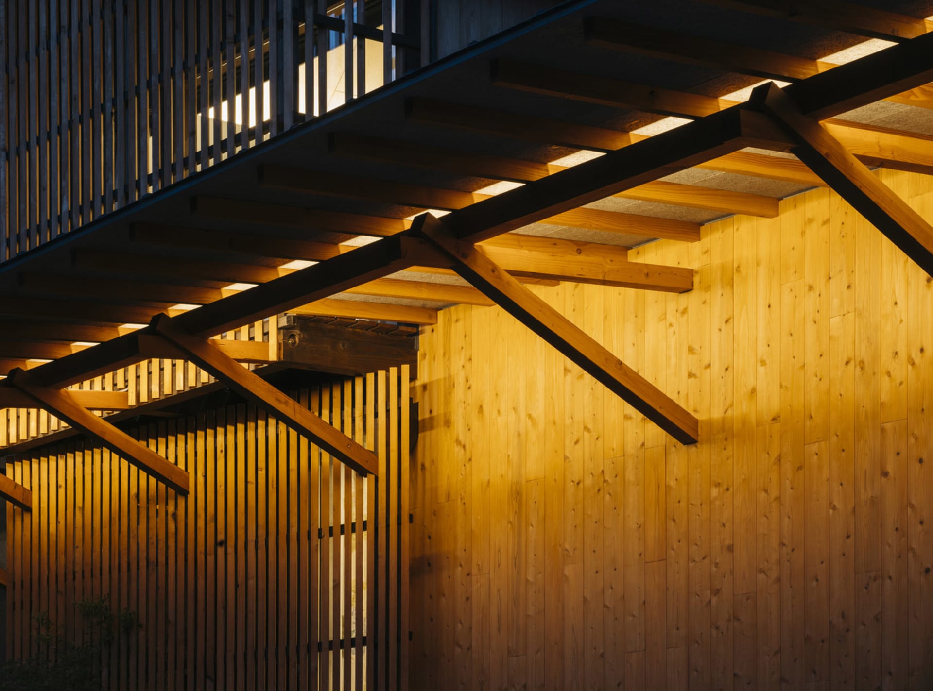 A modern building exterior composed of wooden elements and beams illuminated by warm lighting.