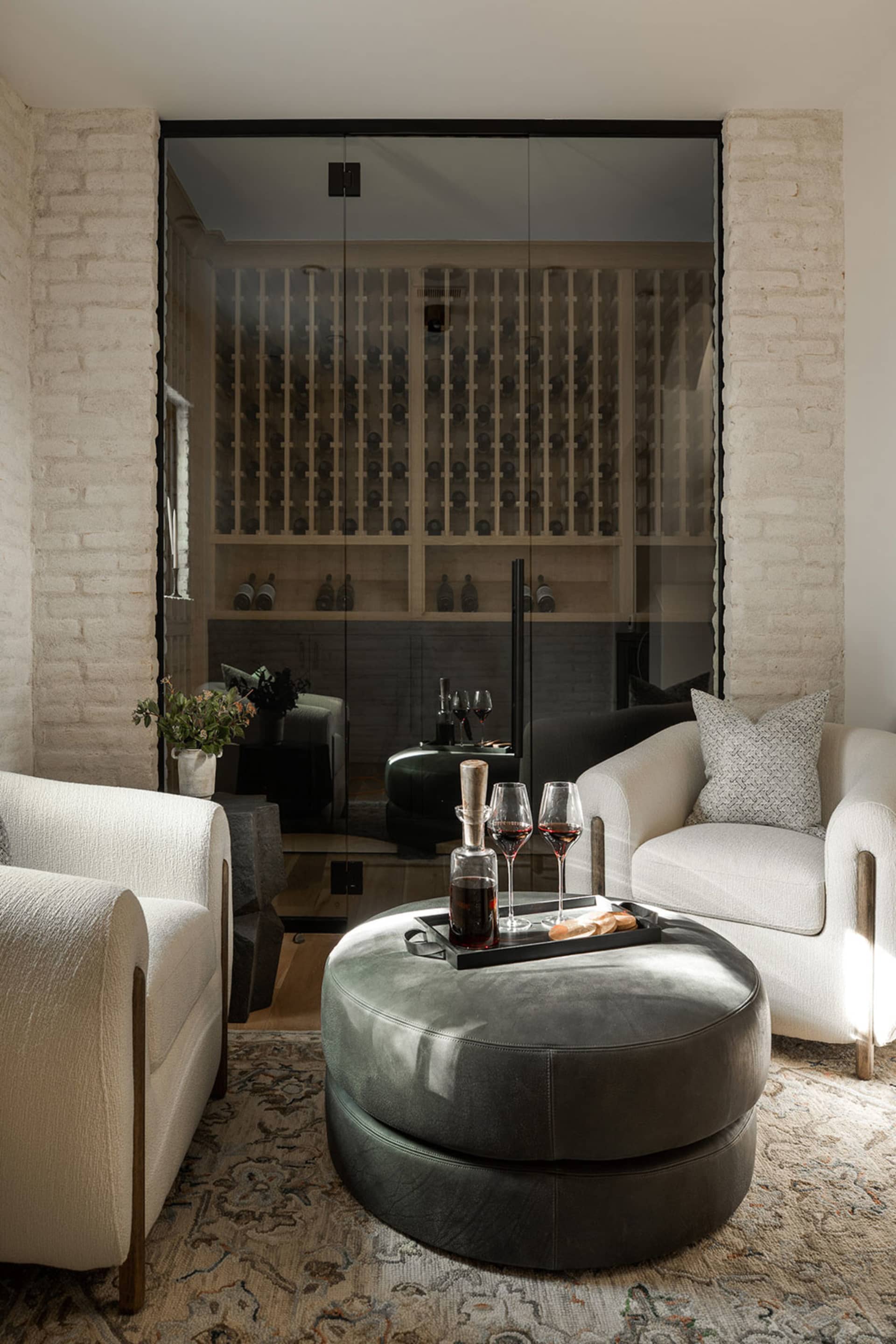 A modern living room featuring a black leather ottoman with a glass top, a small wooden side table, two off-white armchairs w