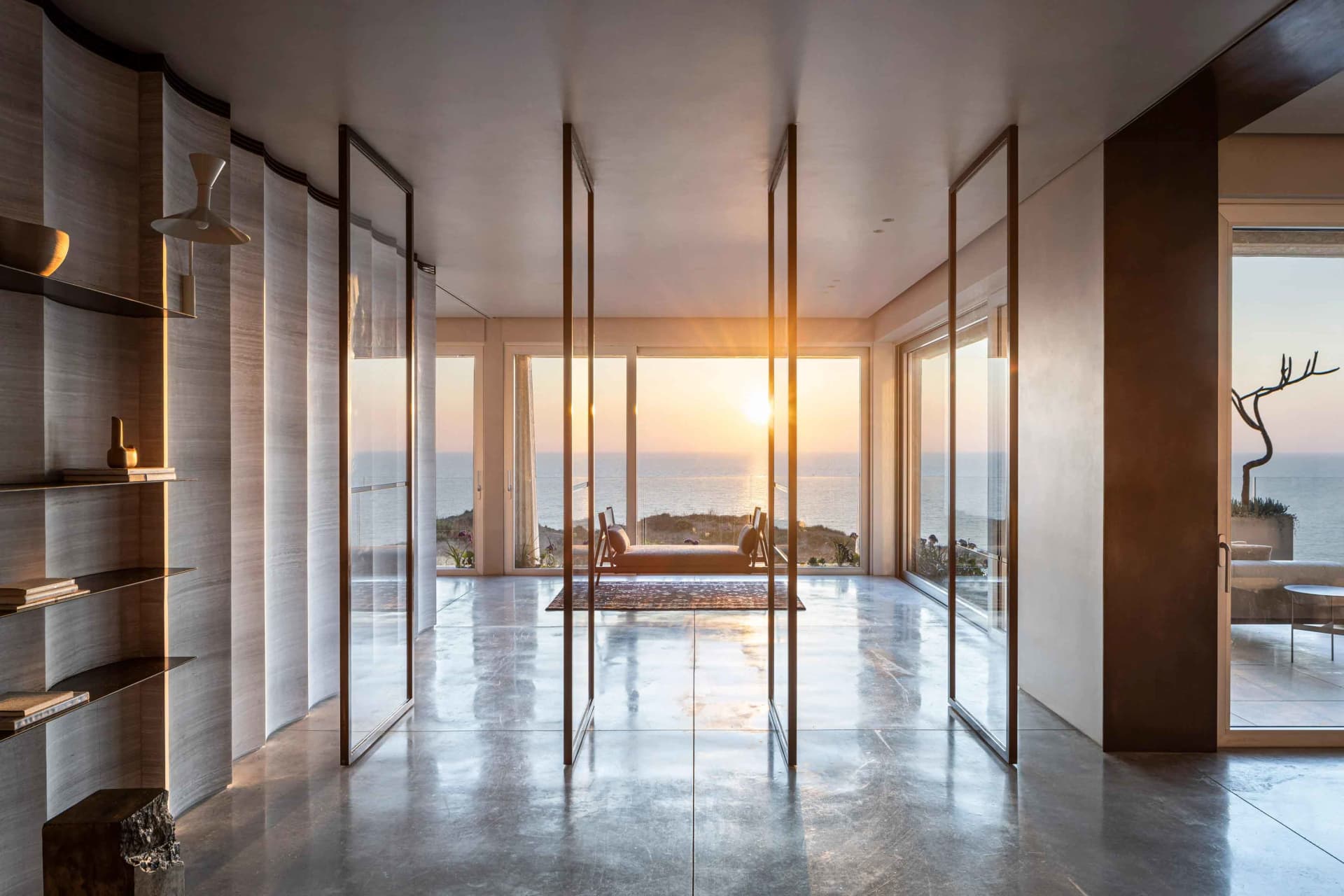 Sunlit room with concrete floor, glass walls, and ocean view.