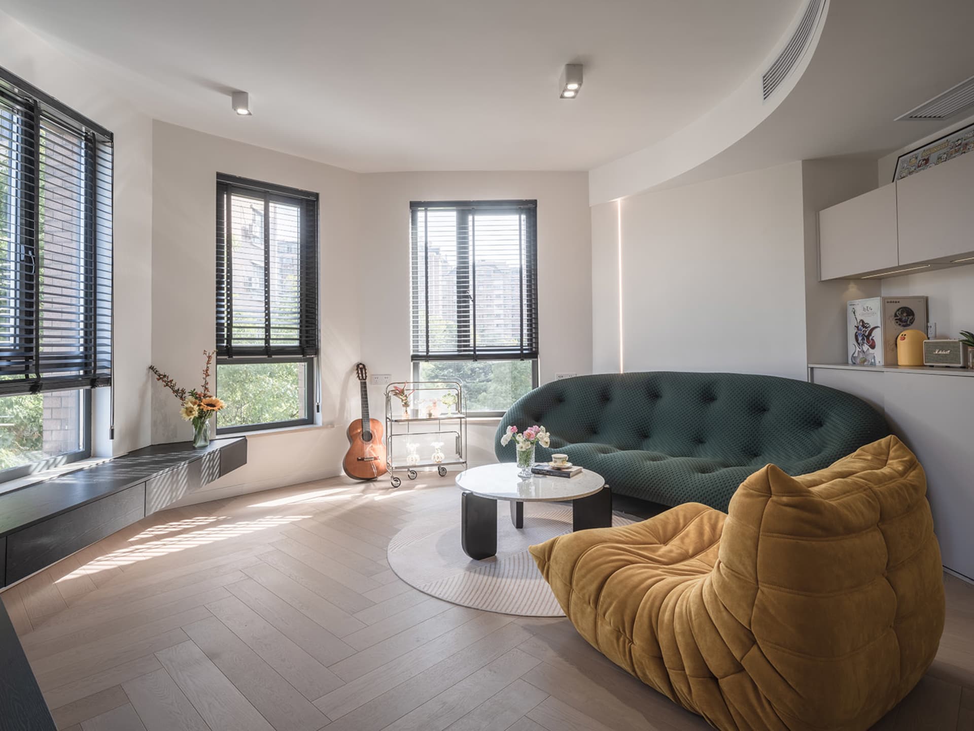 A modern living room featuring minimalist furniture, large windows, and a wooden floor with sunlight streaming through.