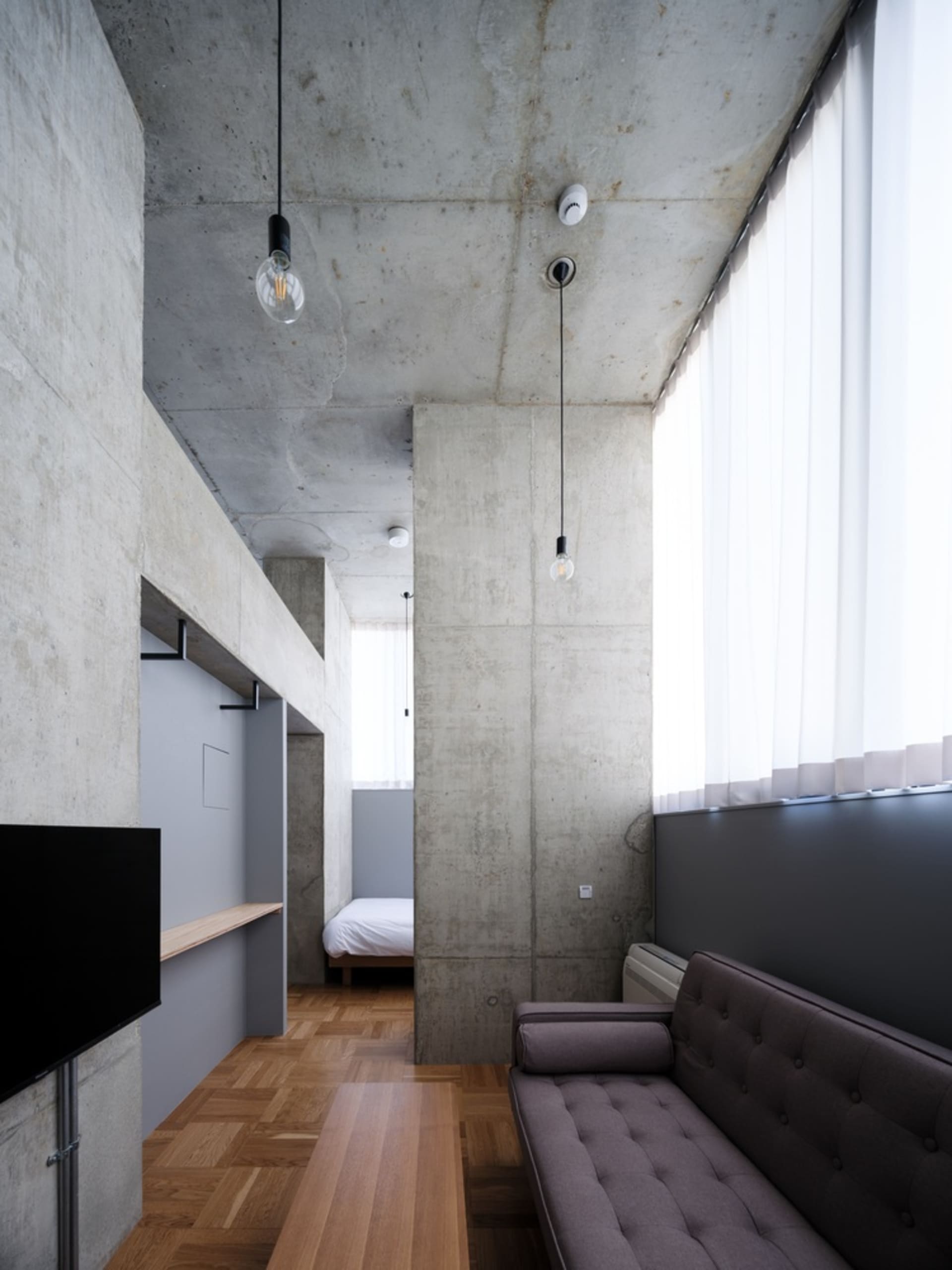 A minimalist living room with concrete walls and a large window.