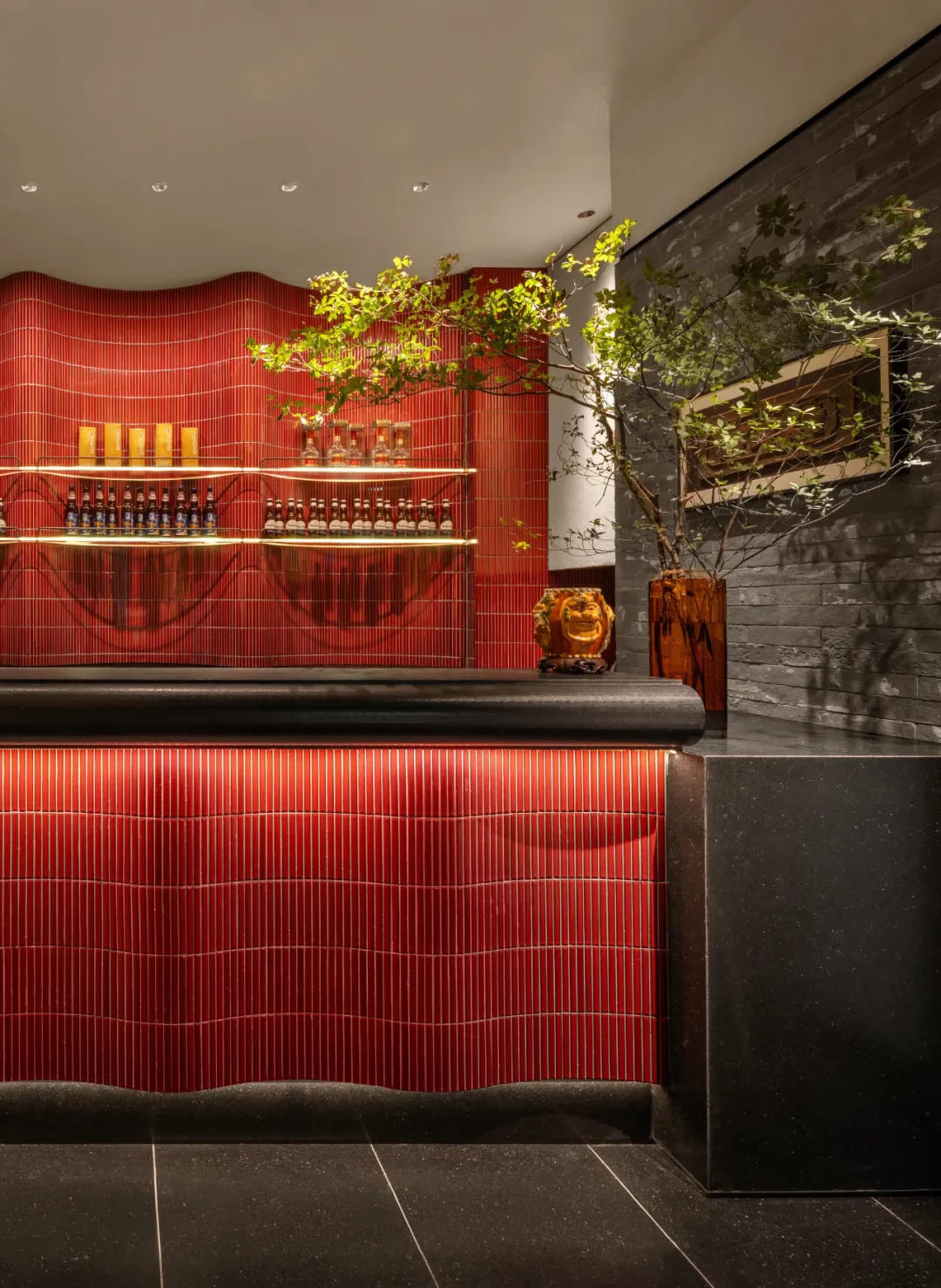 A cozy bar area with a red countertop, striped wall, and wine glasses, vases, and bottles arranged on the counter