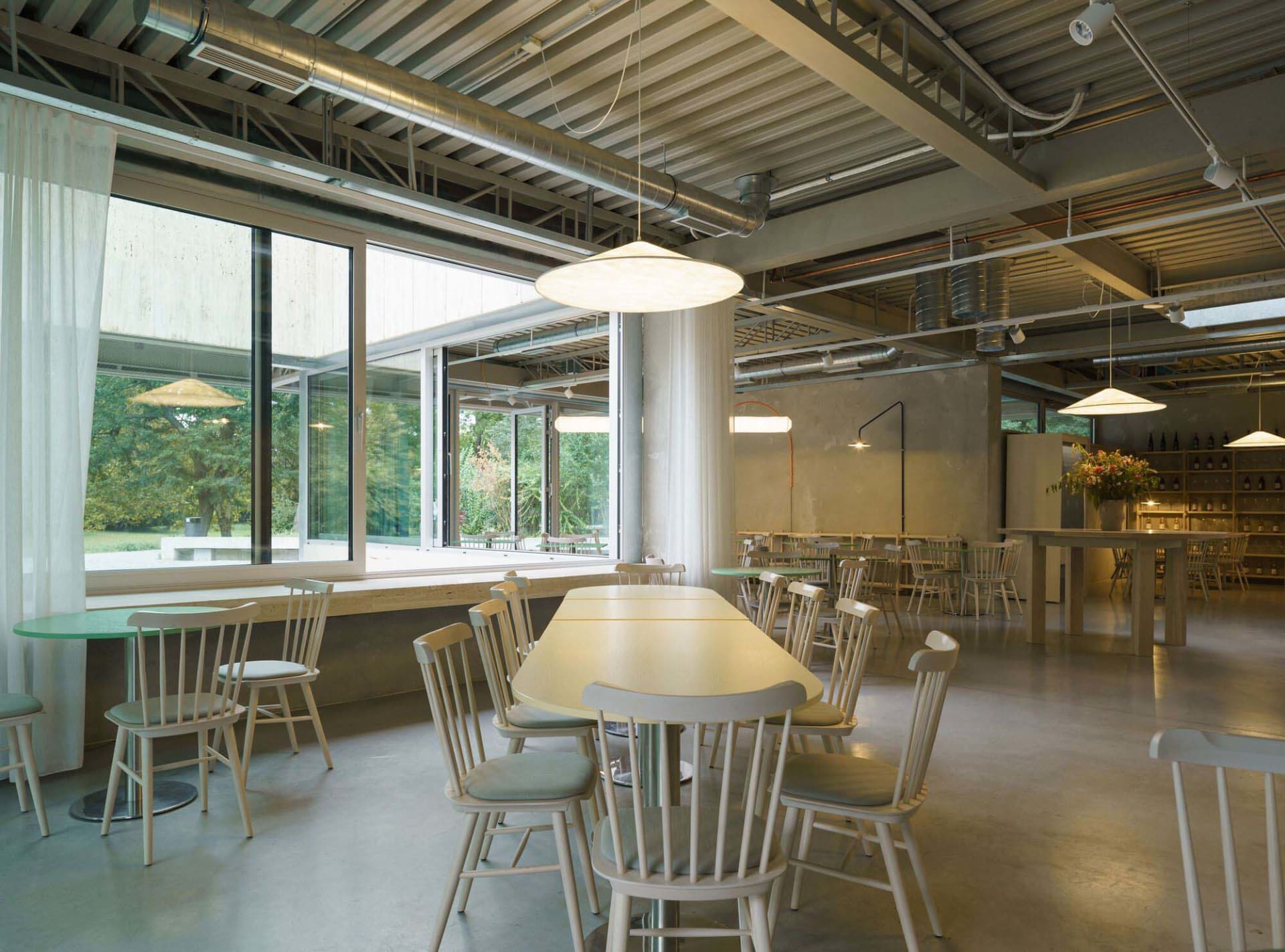 Inviting restaurant interior with a large wooden dining table surrounded by white chairs, potted plants, and ample seating options