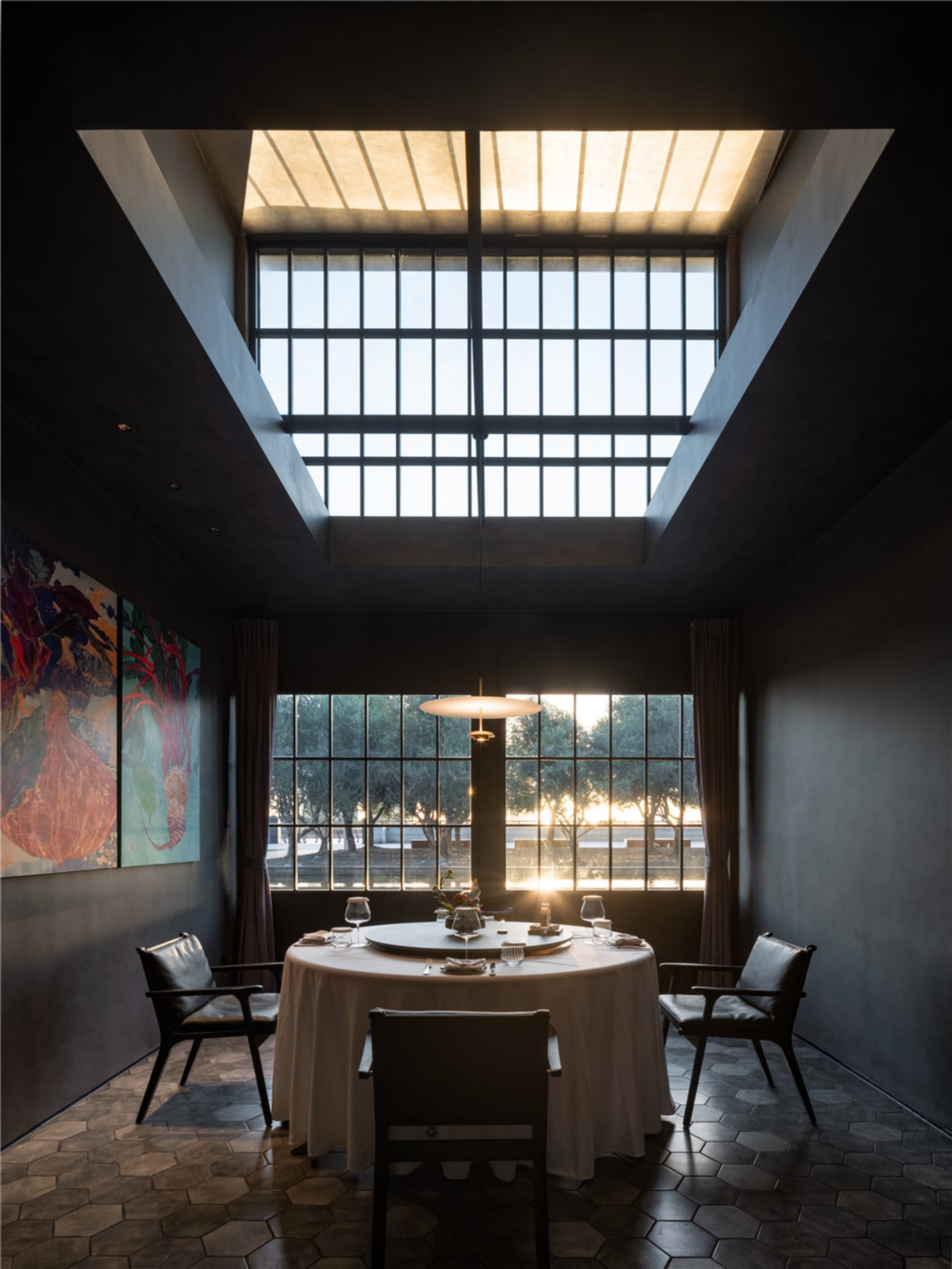 Dining area with two chairs around a round table, white tablecloth, and large window allowing sunlight to enter, creating a warm atmosphere