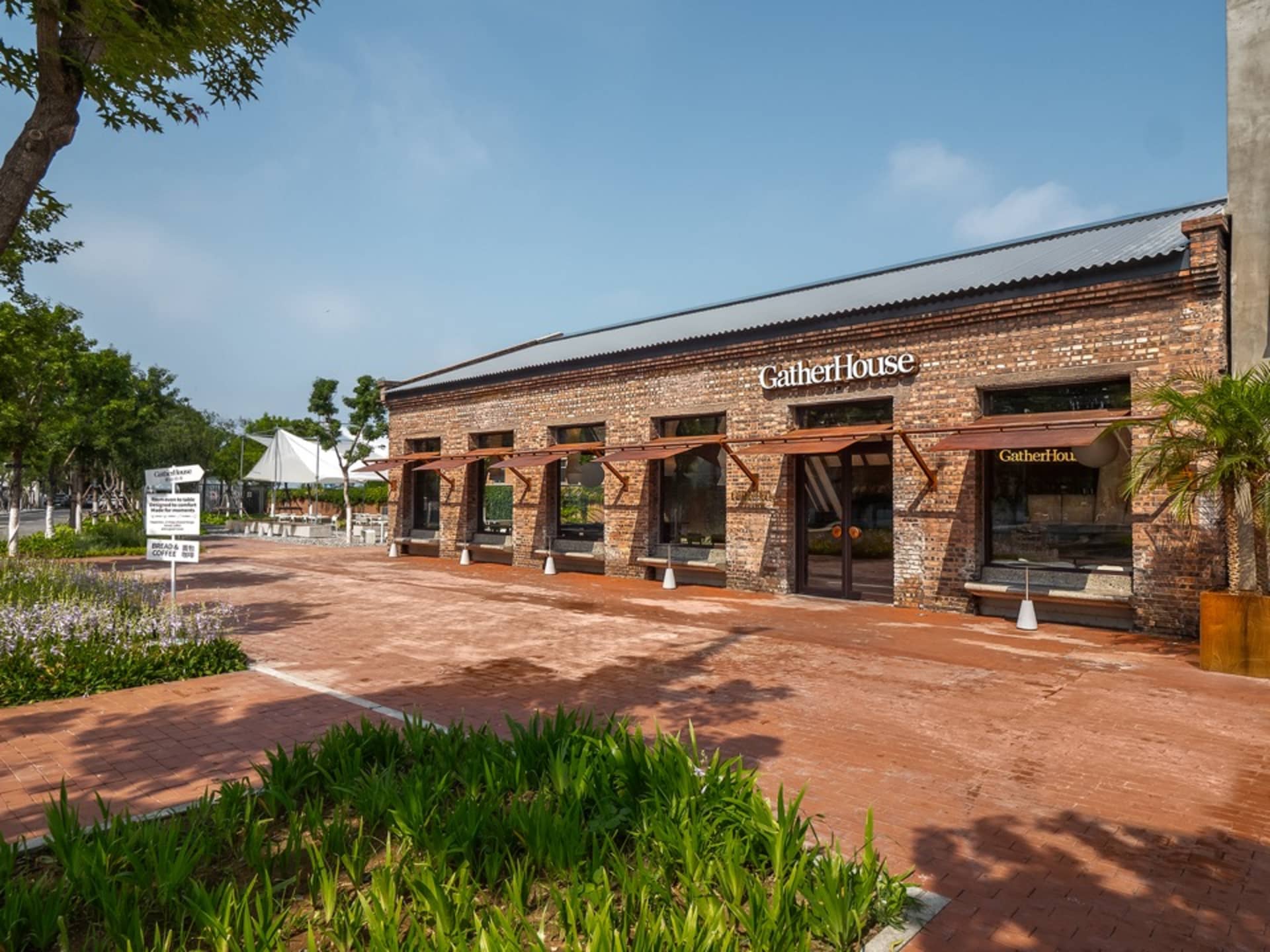 A rustic restaurant with a red roof and brick walls, featuring umbrellas and chairs outside, creating a warm and inviting atmosphere