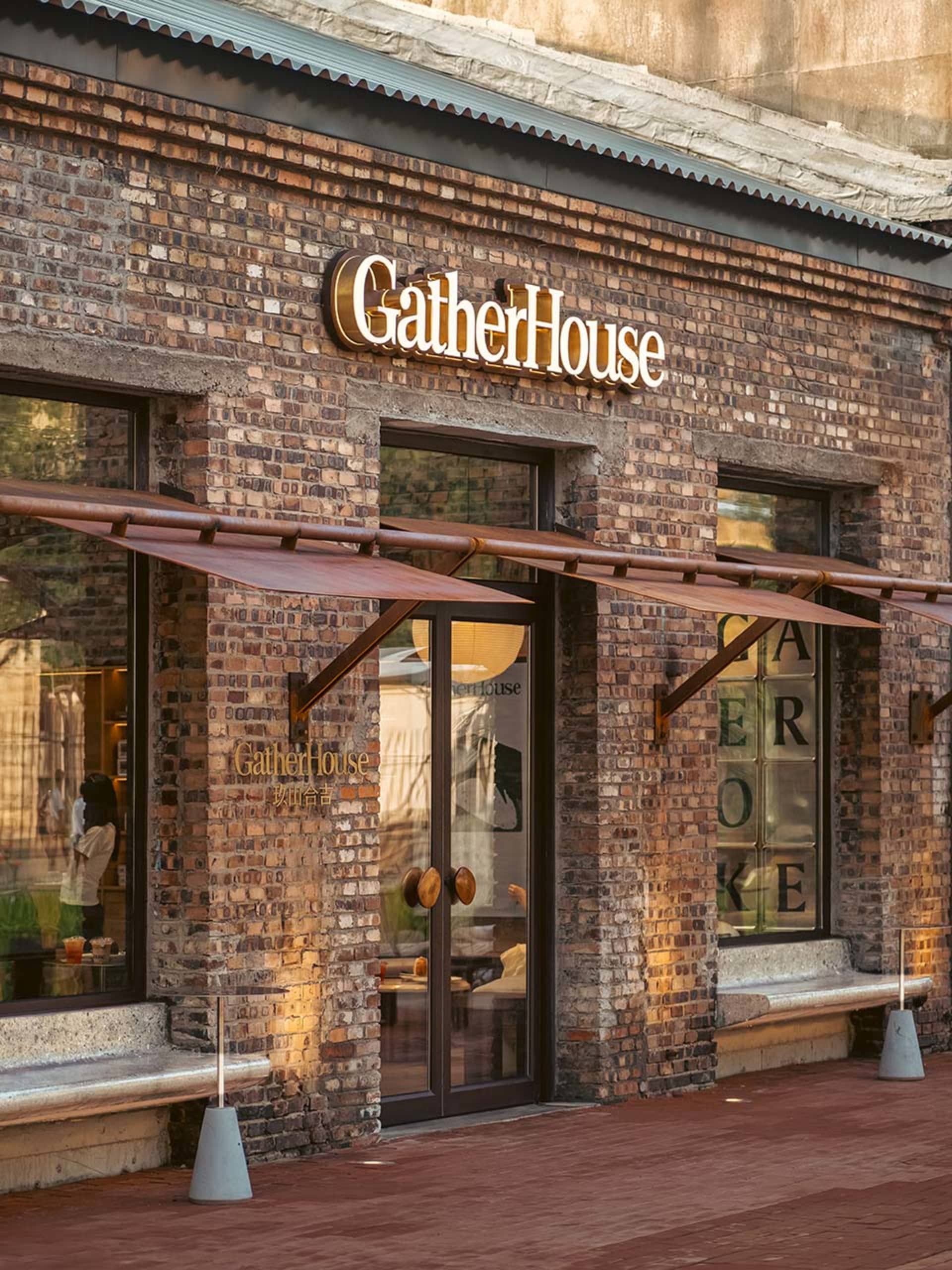 A traditional storefront with a brick exterior and a cozy interior featuring chairs and natural/artificial lighting