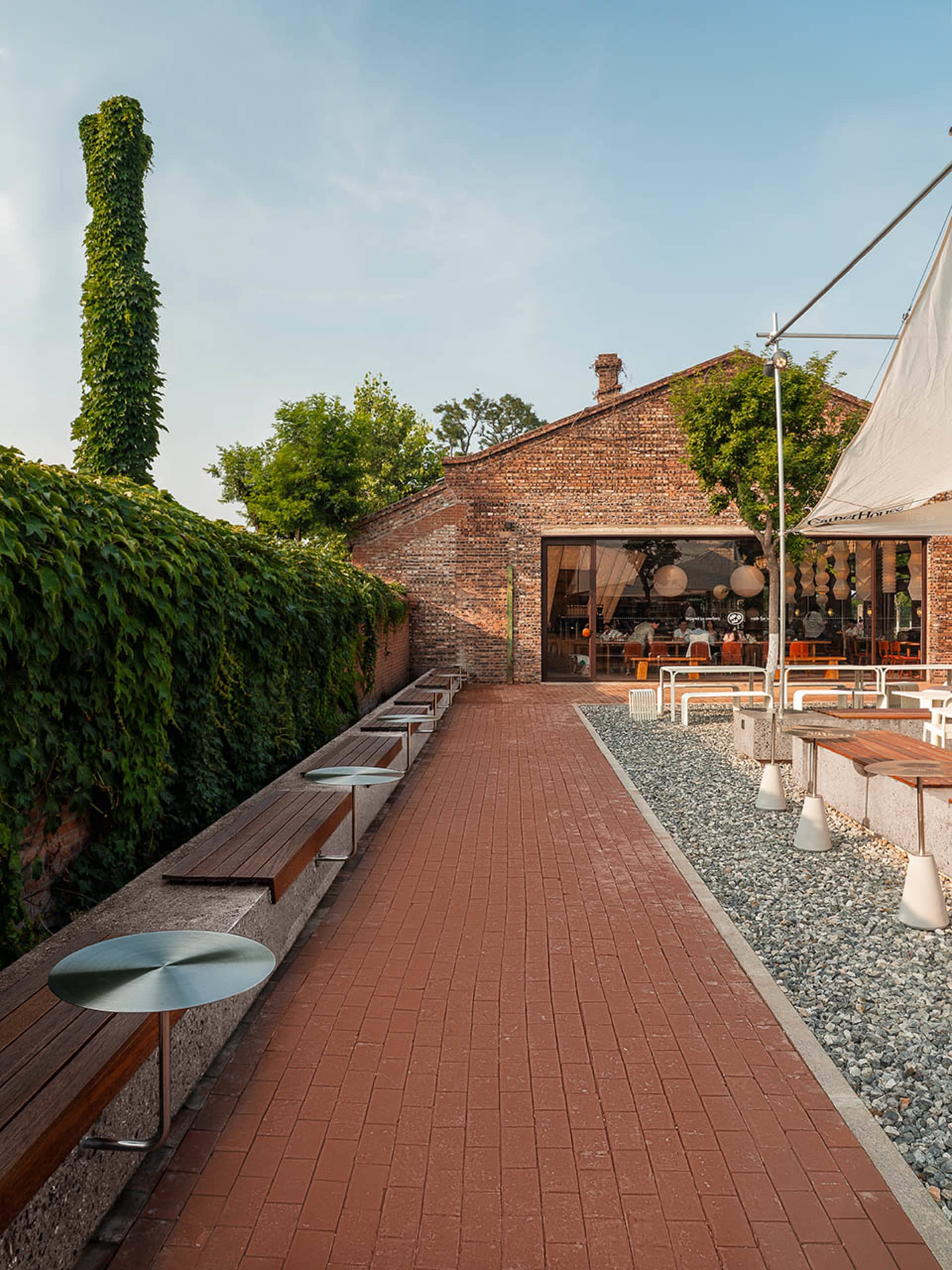 A brick walkway surrounded by dining tables, chairs, and benches in an inviting outdoor patio area