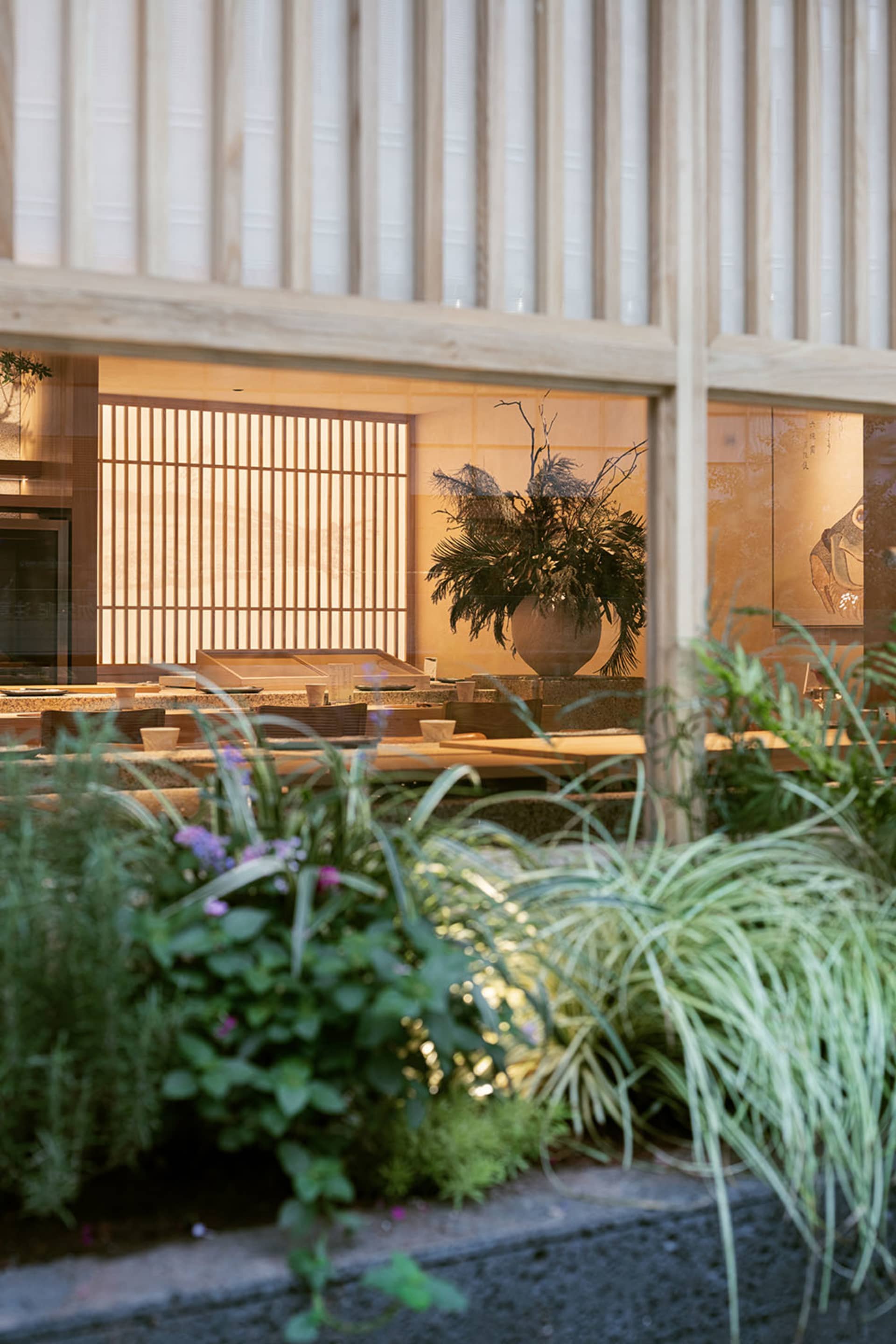 A modern restaurant interior with a dining table, chairs, and potted plants, creating a cozy atmosphere
