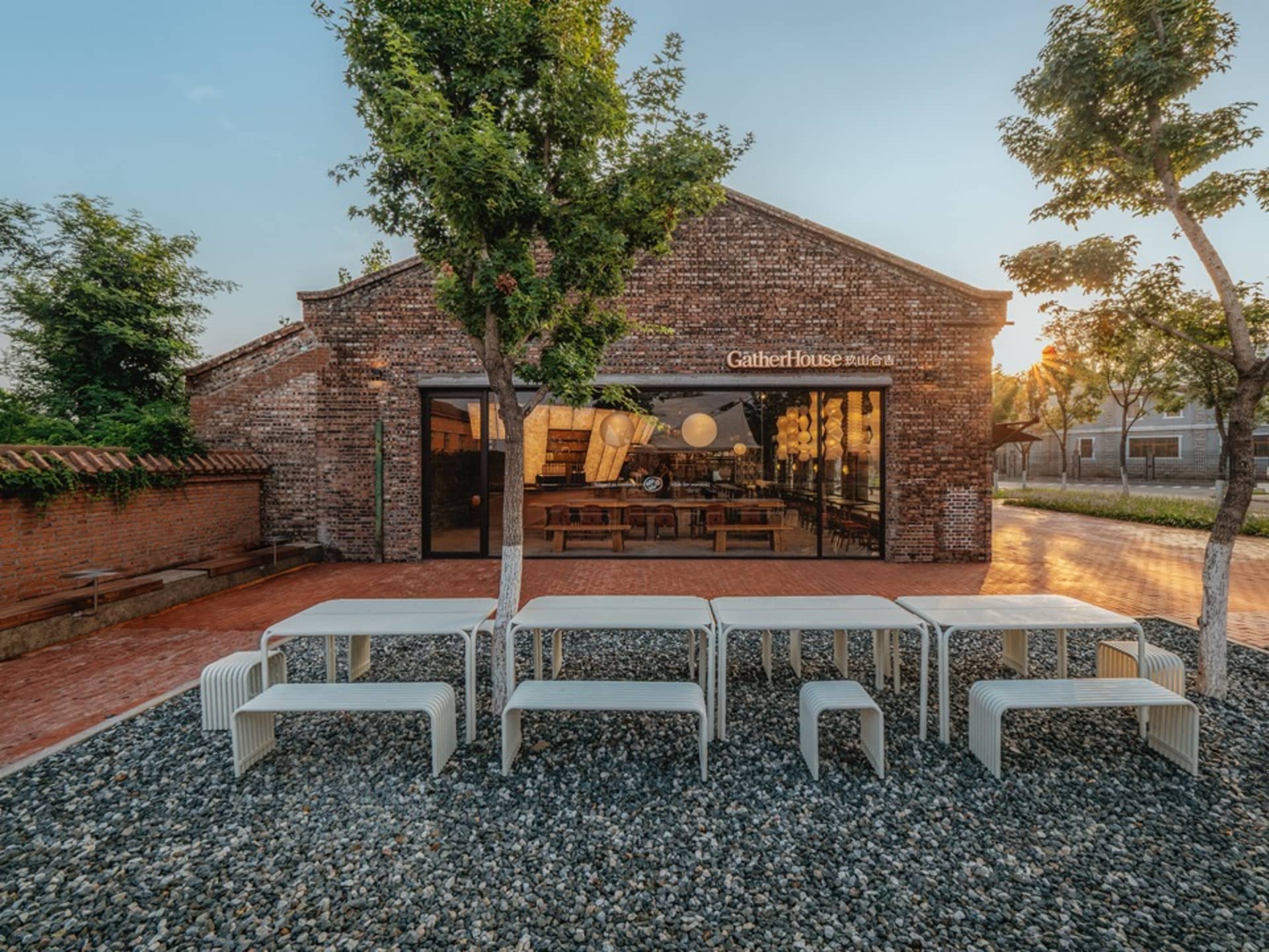 A brick restaurant building with a patio area featuring white tables and chairs, umbrellas, and a welcoming atmosphere