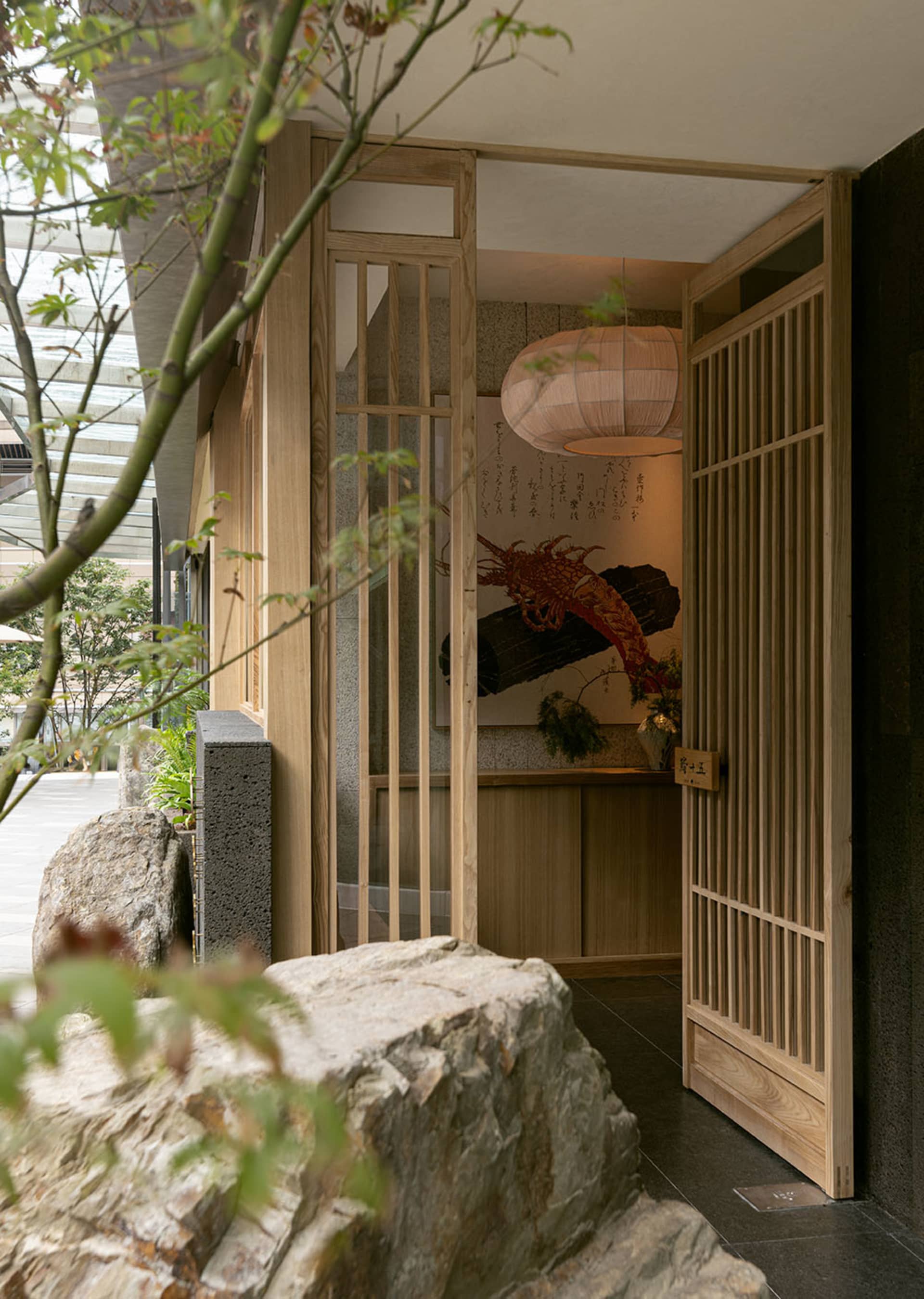 Asian-style interior design with wooden doors, stone walls, and a rock wall, featuring a potted plant and two large rocks