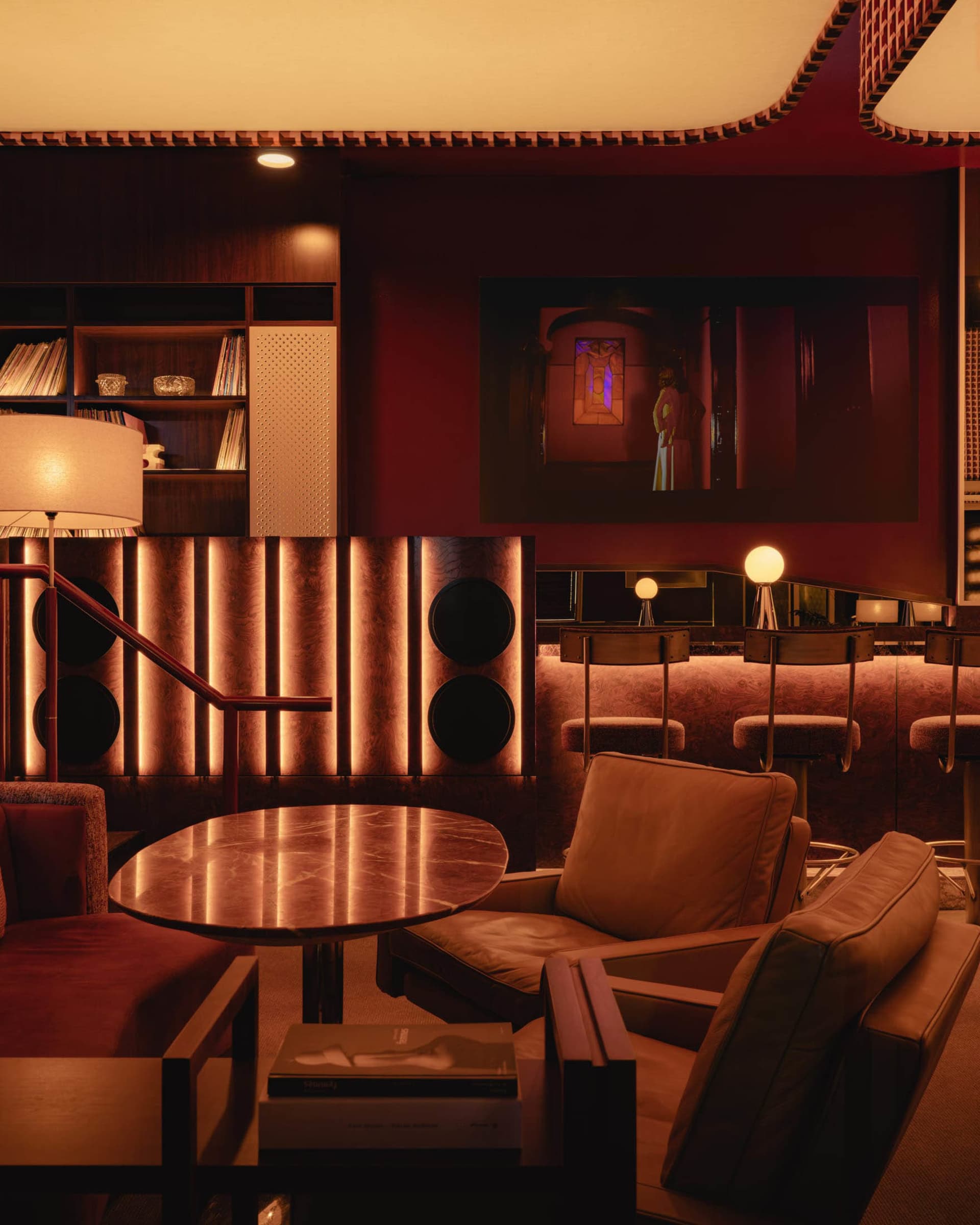 A living room with a red accent wall, multiple chairs, a dining table, a couch, a TV, and books, creating a cozy atmosphere for relaxation and reading