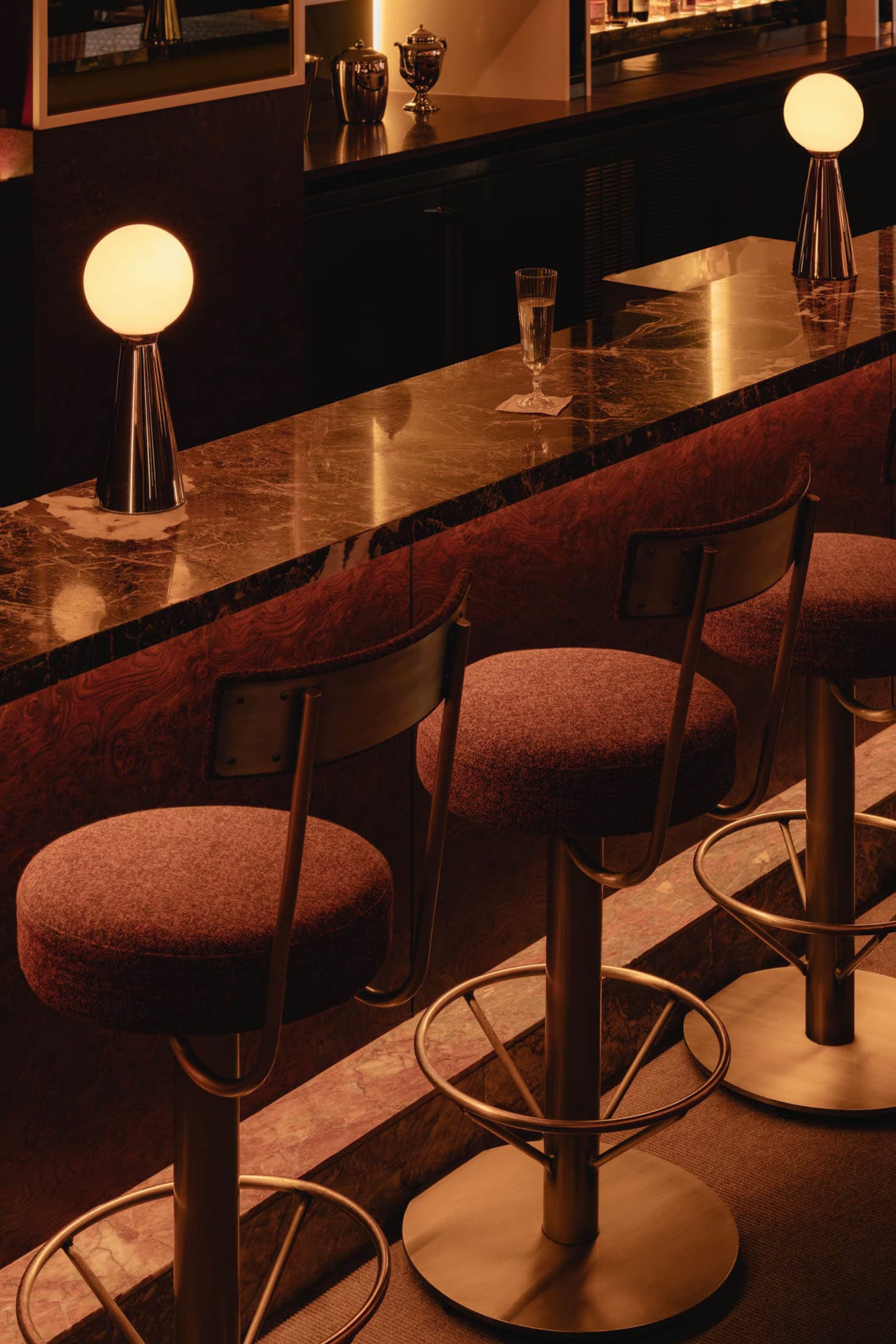 Elegant bar area with a marble countertop, three stools, and a dining table, lit by a circular light fixture