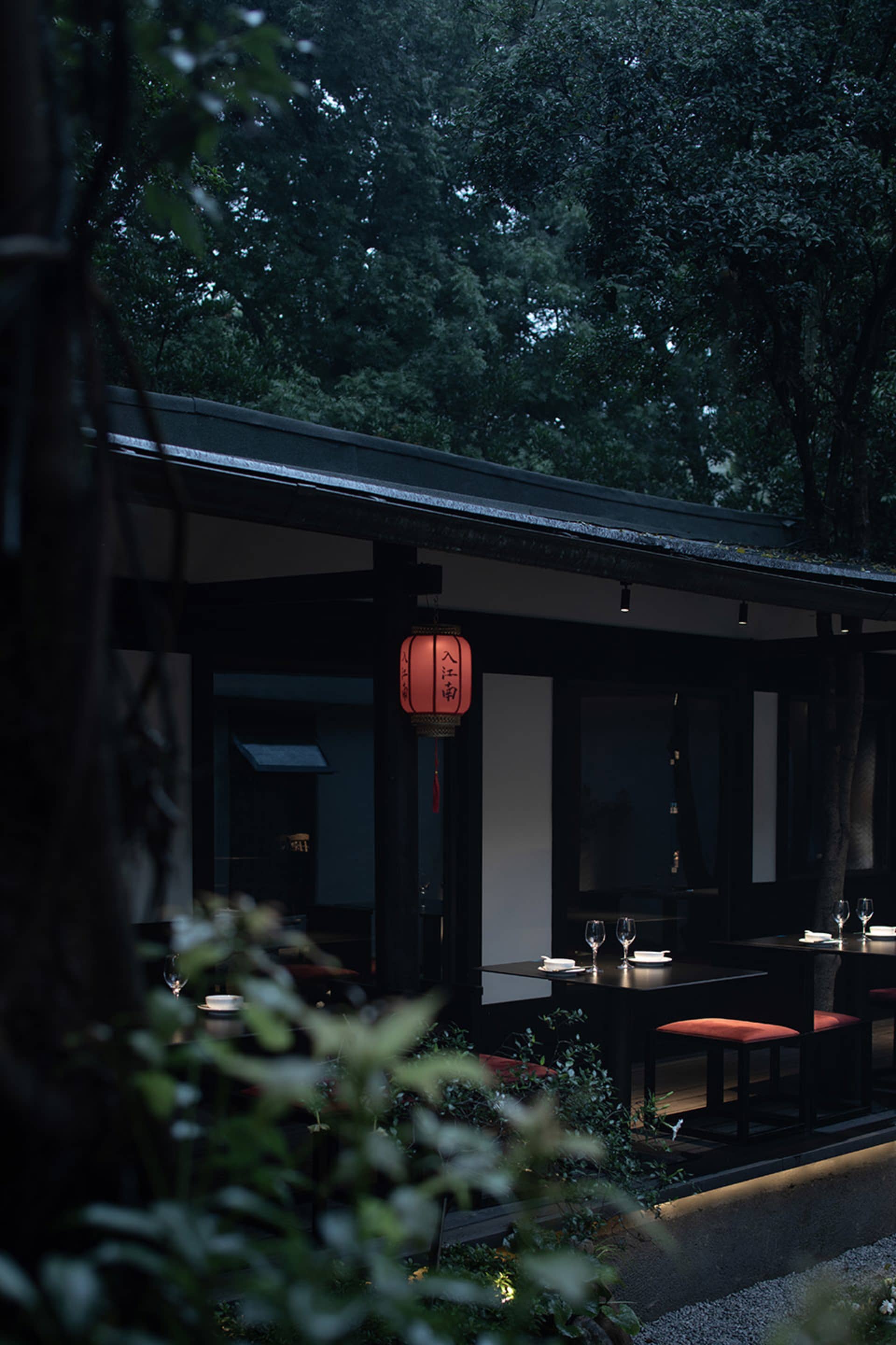 Modern restaurant interior with black walls, a red accent wall, and dining tables with wine glasses