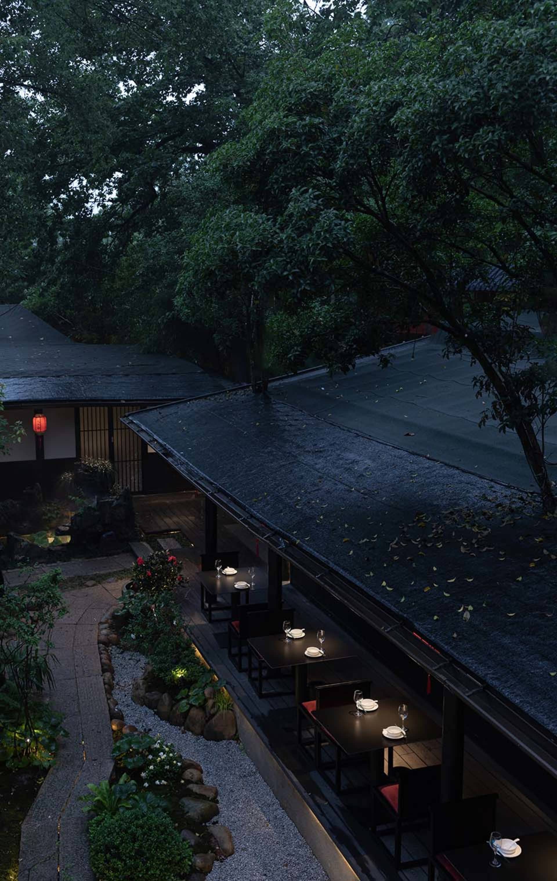 Cozy Asian restaurant with a black roof, red trim, and potted plants, featuring a dining area with tables and chairs and wine glasses