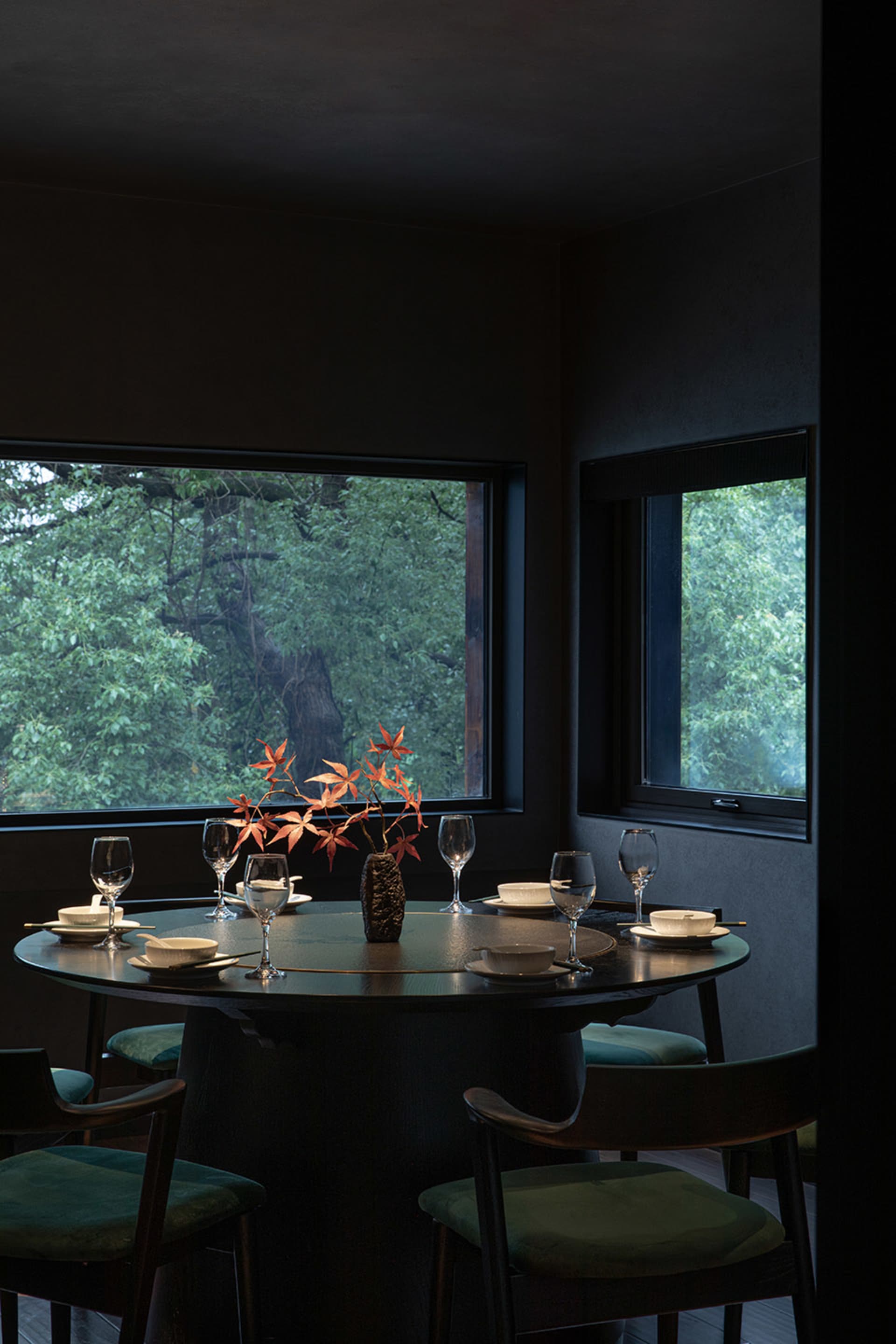 A dining area with a round table, chairs, wine glasses, and vases in a darkened room, creating an intimate atmosphere