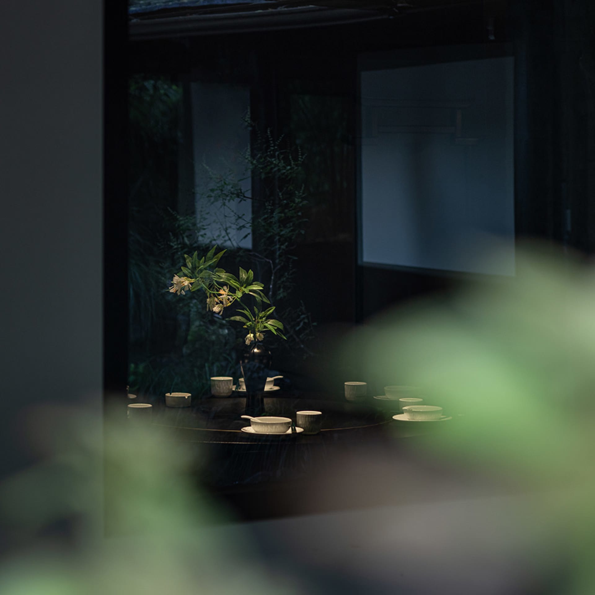 A warm and inviting dining area with a table, chairs, and a vase with flowers, surrounded by plants and tableware